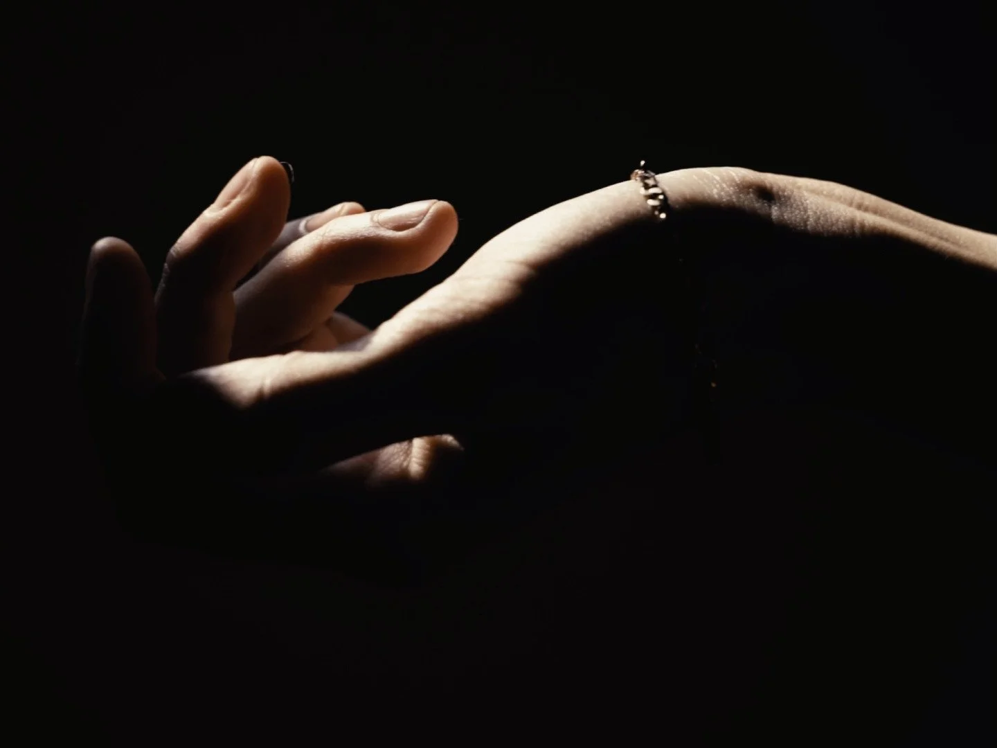 Close-up of a person's hand with a ring, illuminated against a dark background.