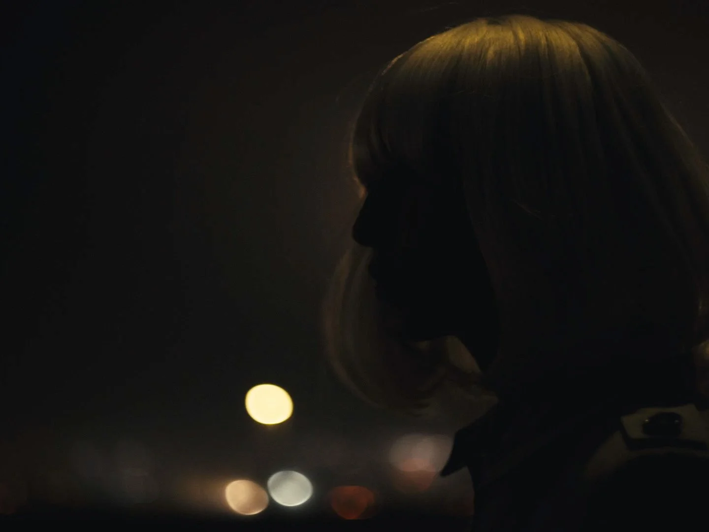 Silhouette of a woman with long flowing hair against a dark background with blurred bokeh lights.