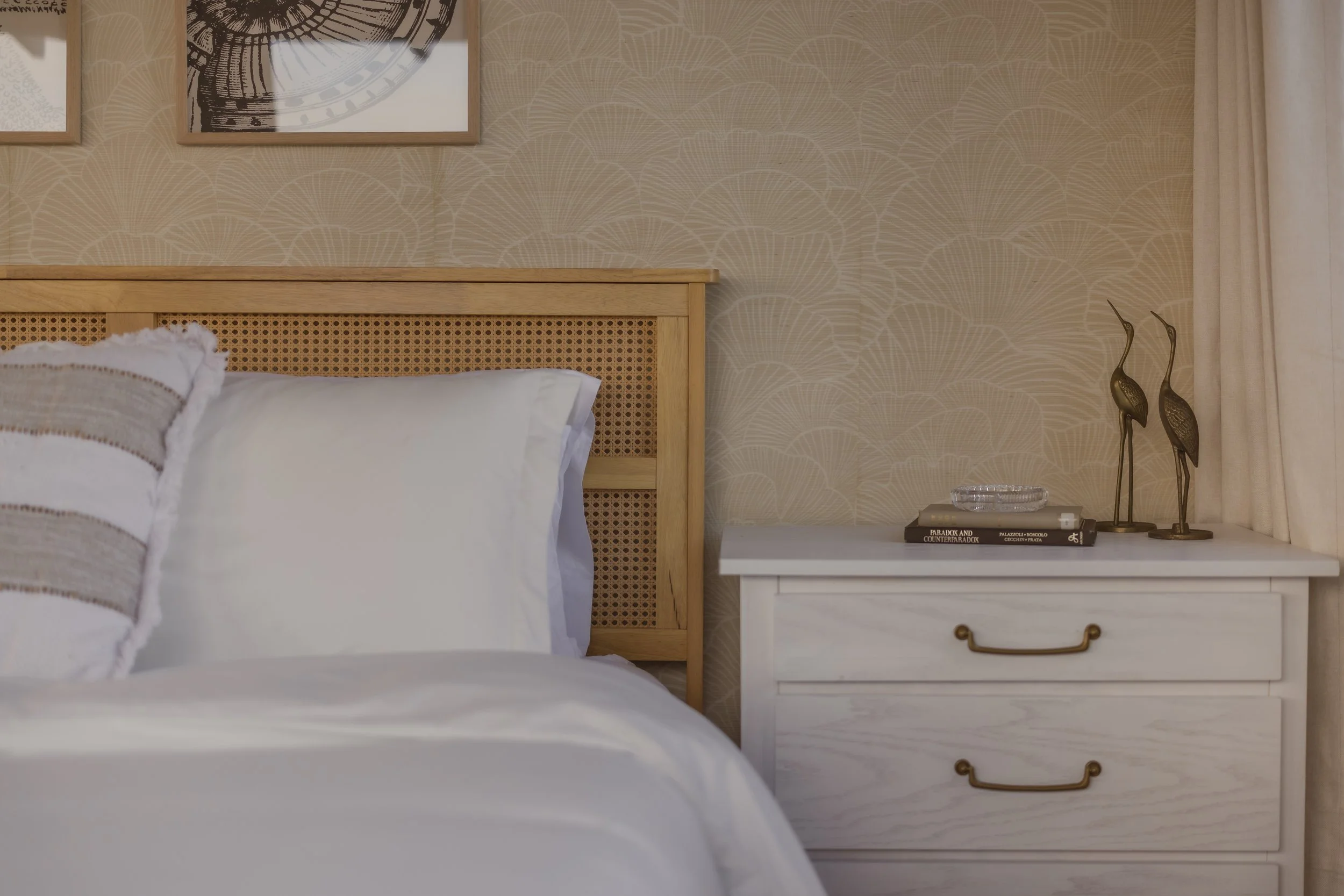 Photograph of a seashell bedroom with white night stand, rattan headboard, seashell wallpaper, thrifted books