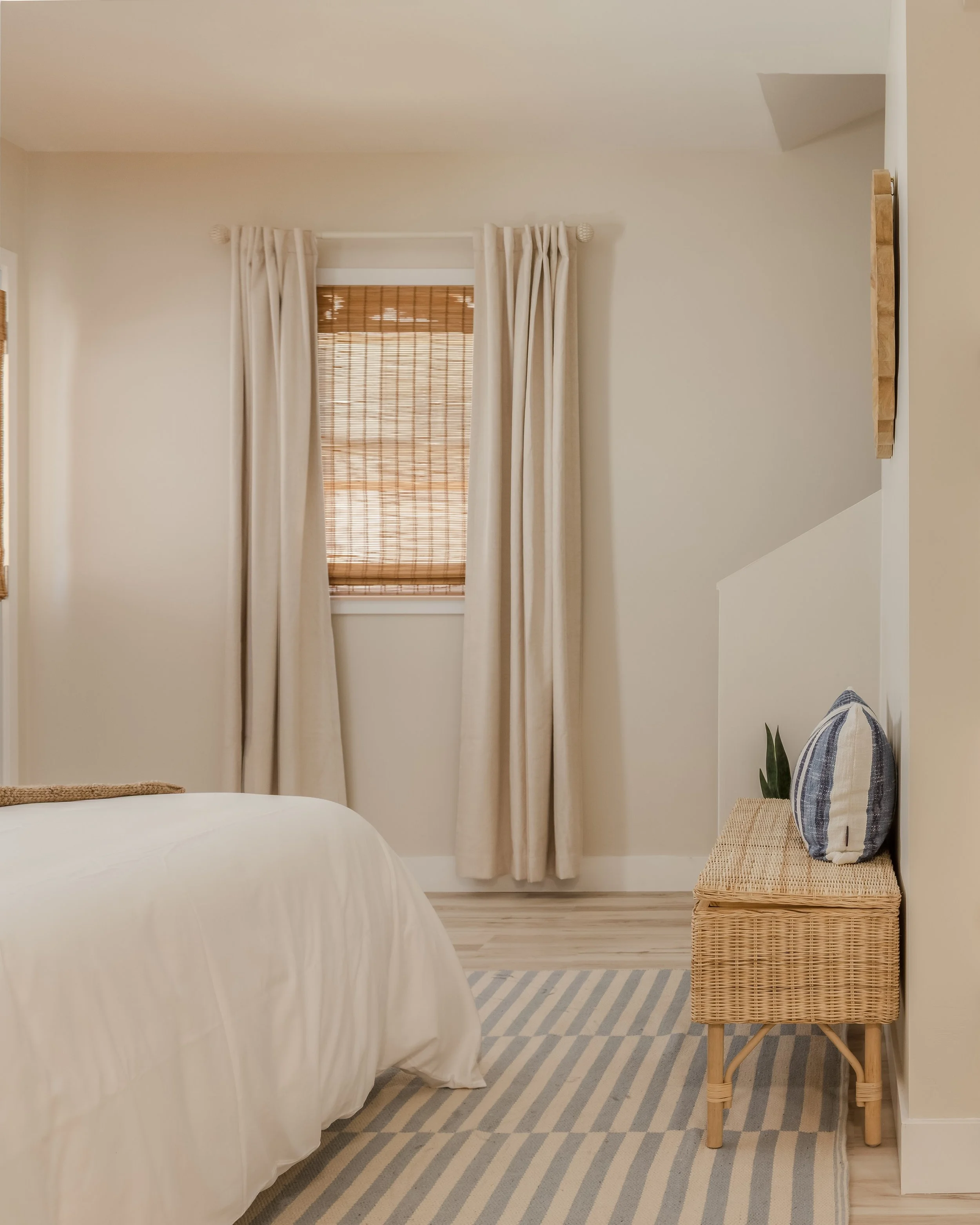 Ocean themed bedroom rattan bench, bamboo blinds, blue striped pillows and rug, fake plants, scalloped mirror