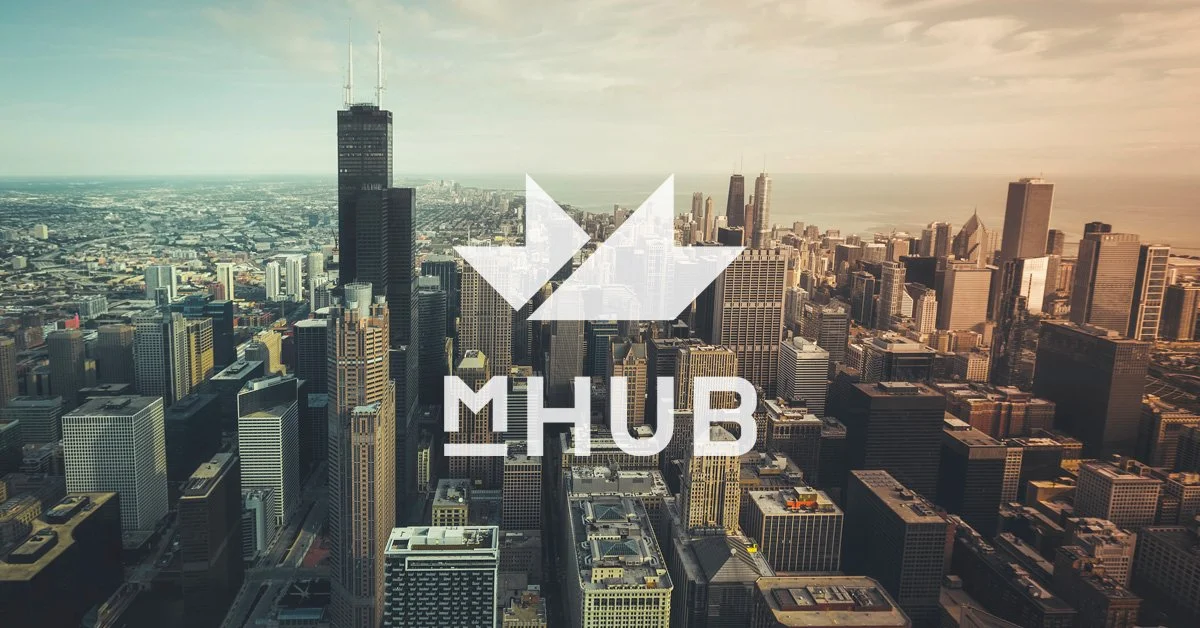 Aerial view of a city skyline with skyscrapers, including the Willis Tower, during sunset or sunrise. The city is likely Chicago, with Lake Michigan visible in the background. Overlaid on the image is a logo with a white arrow pointing in two directions and the text 'MHUB'.