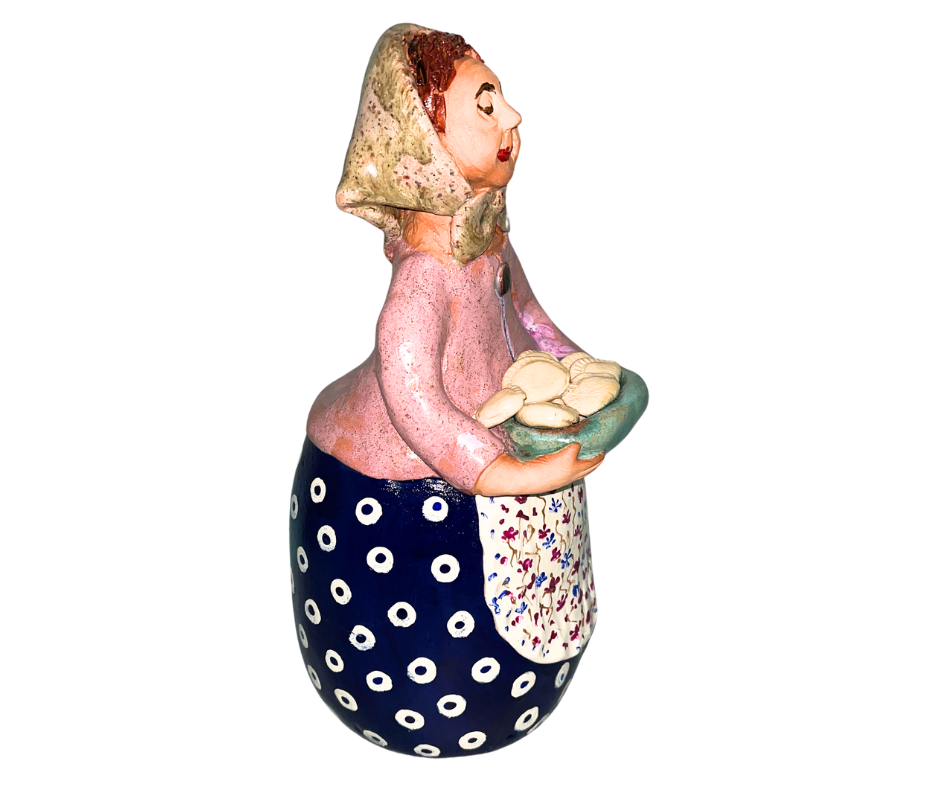 Hand-painted babcia figurine holding a bowl of pierogi, wearing a tan scarf and floral apron