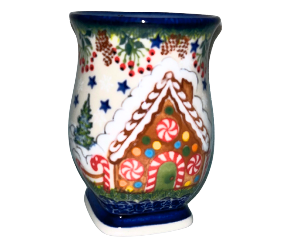 Hand-painted ceramic mug featuring a festive gingerbread cottage surrounded by evergreen branches, berries, and holiday stars. Durable, functional art—perfect for coffee, tea, or seasonal gifting.