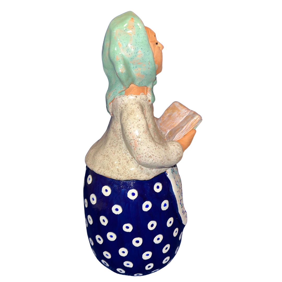 Charming hand-painted “Babcia Holding a Book” figurine featuring a Polish grandmother in an aqua scarf and floral apron. A heartwarming gift and beautiful piece of folk-inspired home décor.