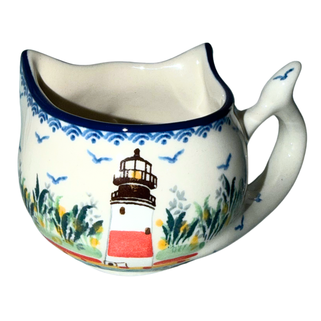Ceramika Artystyczna U5220 Polish Pottery cat-shaped cup featuring a hand-painted lighthouse, coastal grasses and seabirds with a whimsical fish-tail handle.