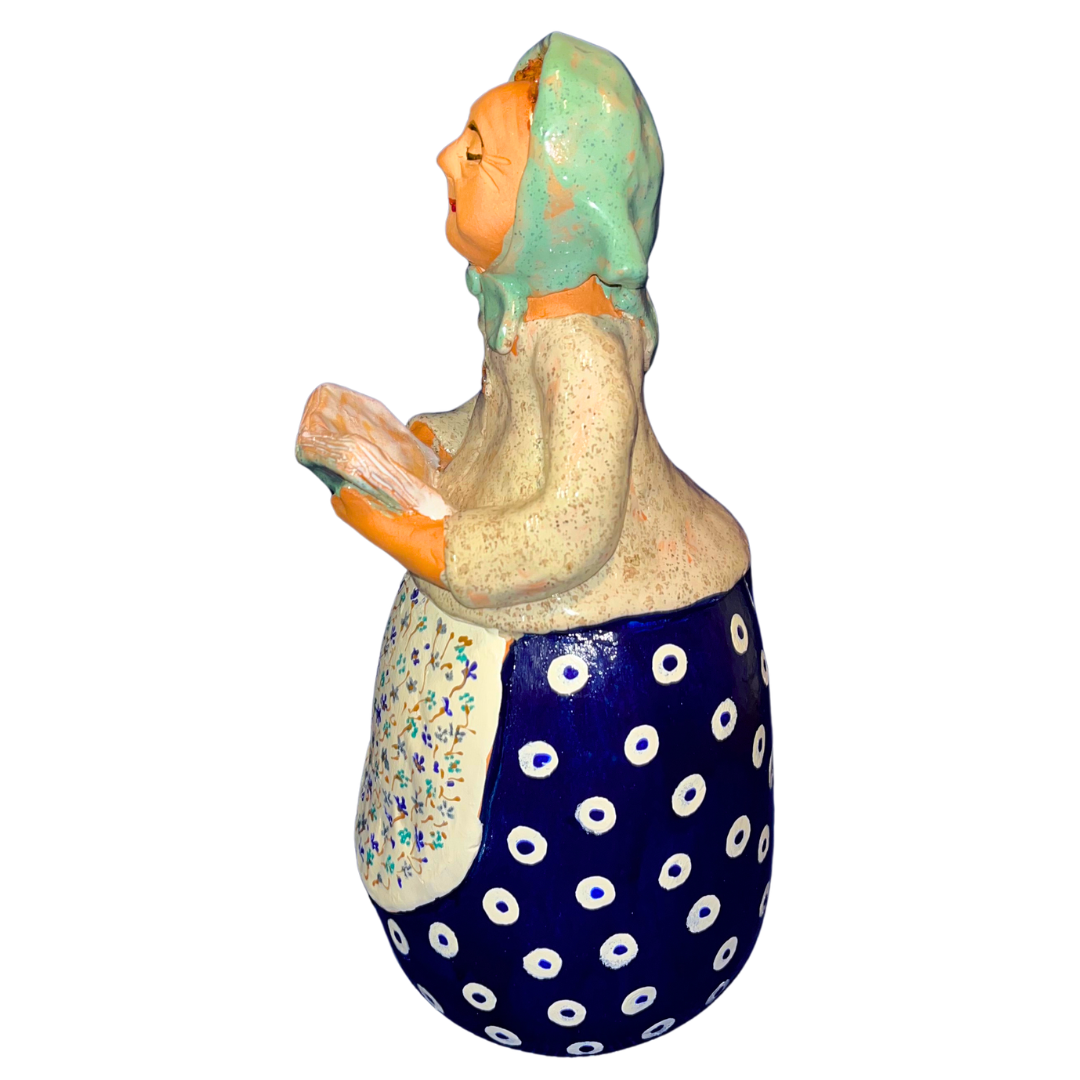 Charming hand-painted “Babcia Holding a Book” figurine featuring a Polish grandmother in an aqua scarf and floral apron. A heartwarming gift and beautiful piece of folk-inspired home décor.