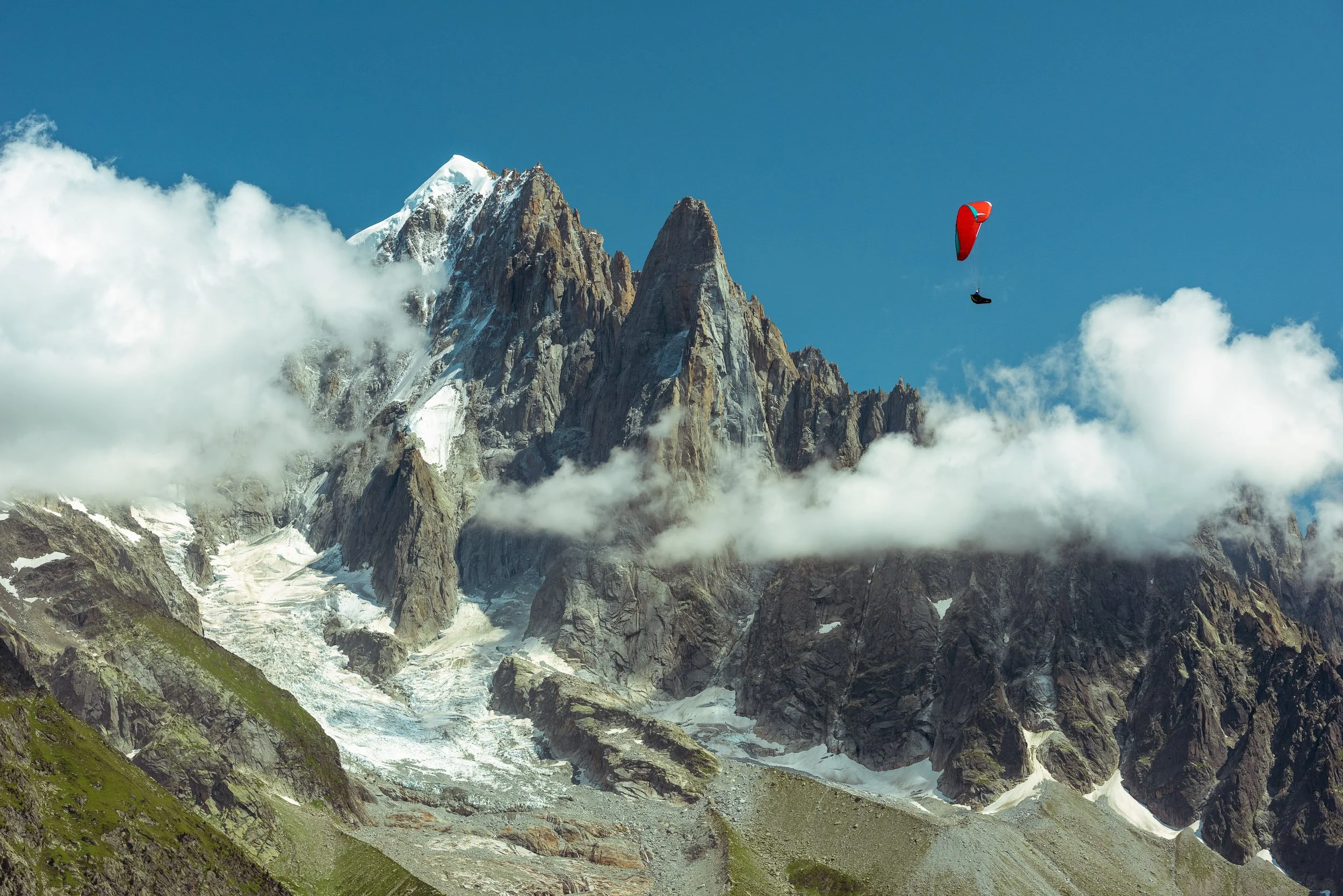 A paraglider flies in front of the iconic peak of Petit Dru (3,733m), one of Aguilles du Dru (Les Drus), in front of a snow-covered Aiguille Verte near Chamonix in France.