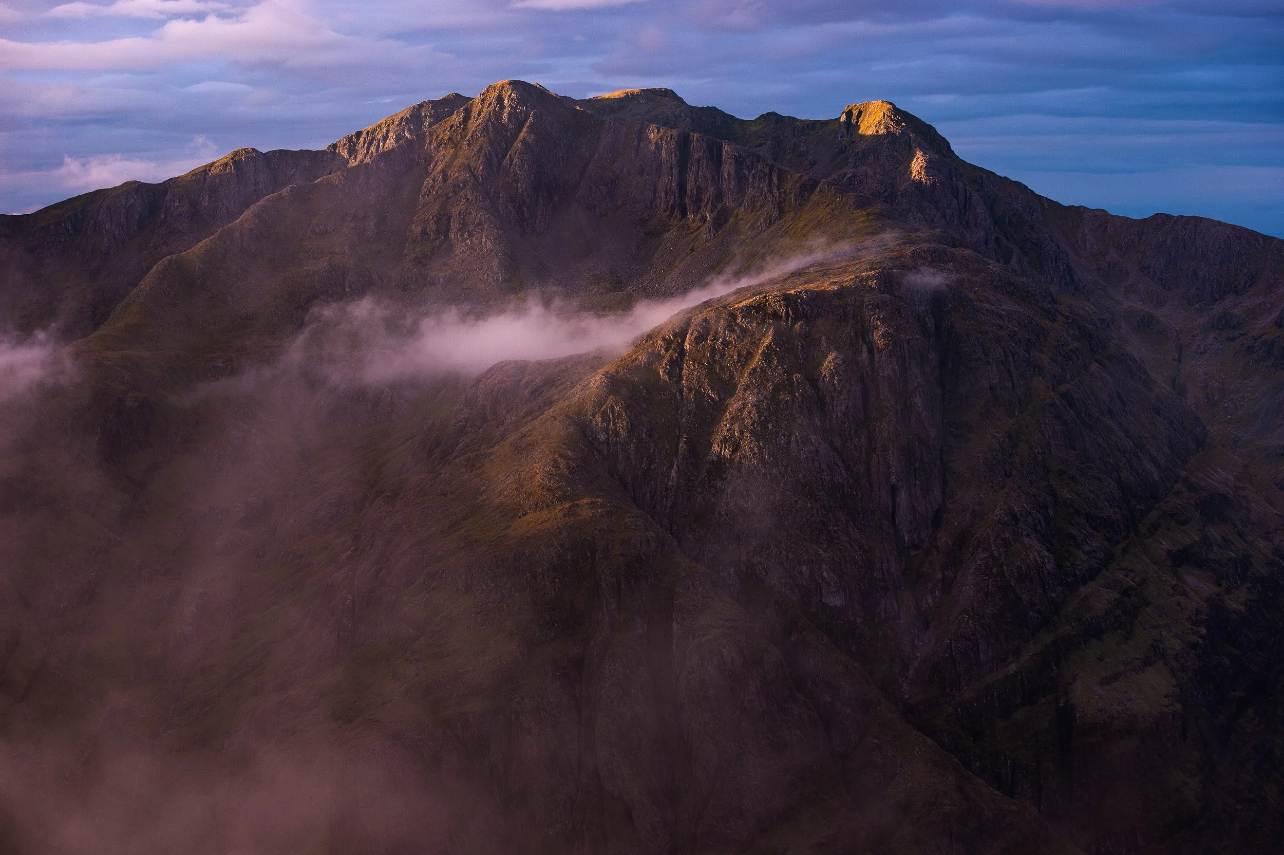 Dawn light illuminates Stob Coire nam Beith summit as clouds fill the corrie beneath Stob Coire nan Lochan on the Munro, Bidean nam Bidean, above Glen Coe, Scotland.
