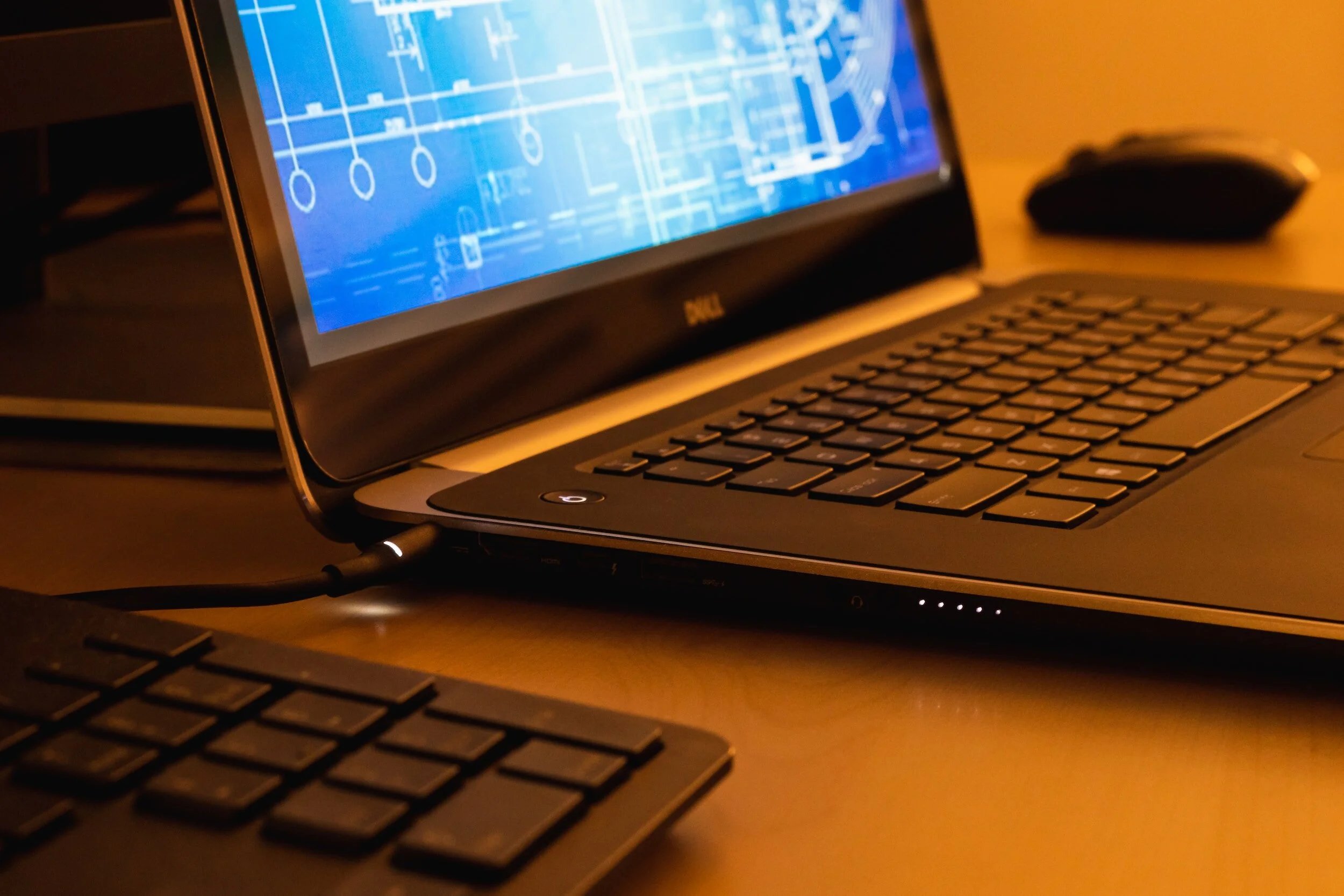 A Dell laptop on a desk displaying a blue technical drawing or blueprint, with a keyboard and mouse nearby.