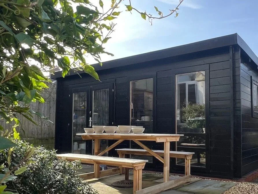 Garden-studio-pictured-behind-a-climbing-clematis-plant-while-drying-her-latest-creations-on-the-picnic-table-on-the-stone-patio