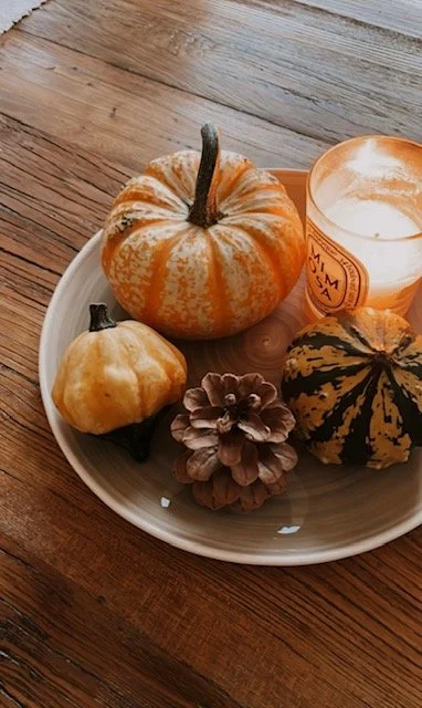 En tallrik med tre små pumpor, ett ljus i ett glas, en tallrik av trä och en träbord.