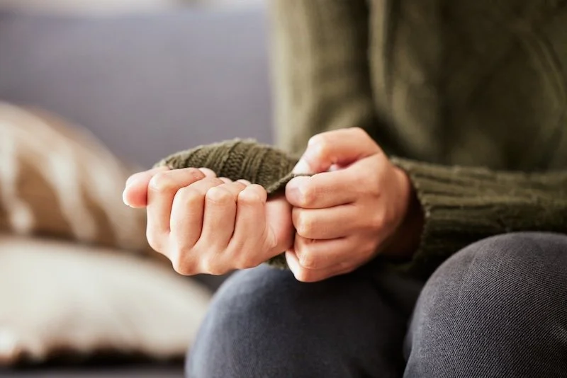 Woman sitting on a couch with hands clasped, showing stress and sadness, representing anxiety and depression counseling and mental health support at home.