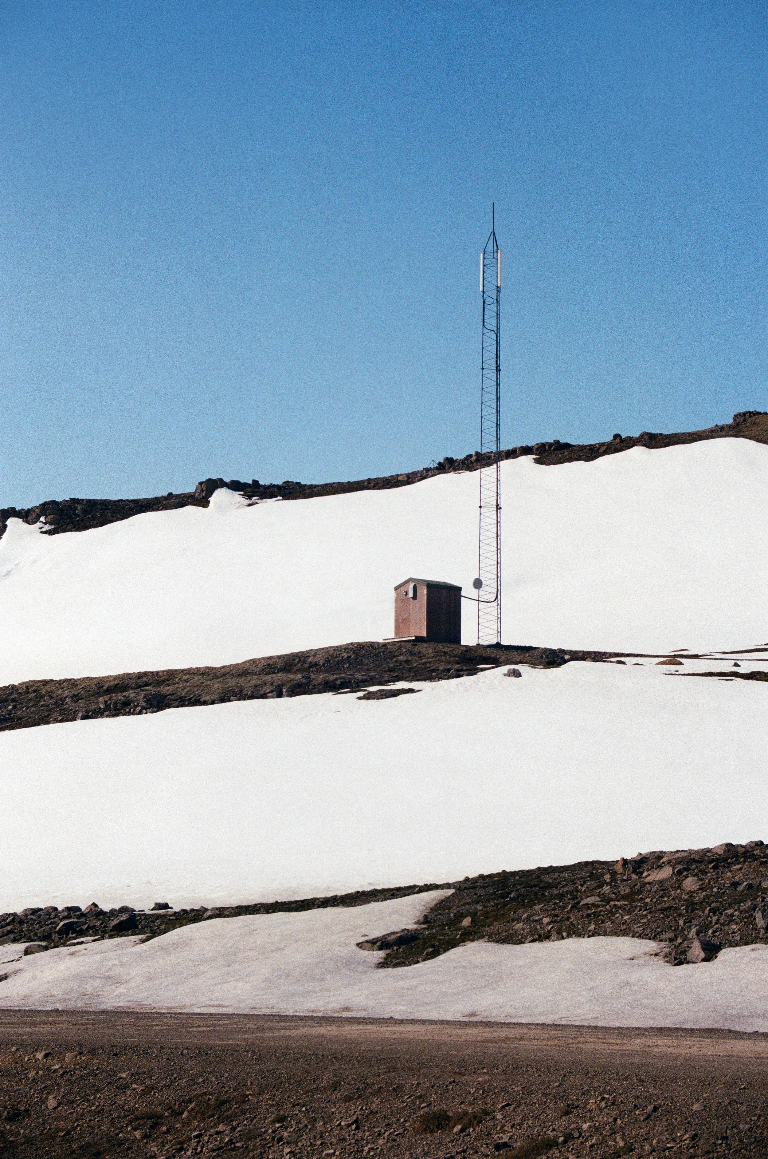 Small hut and radio mast surrounded by snow beneath a clear blue sky in Iceland