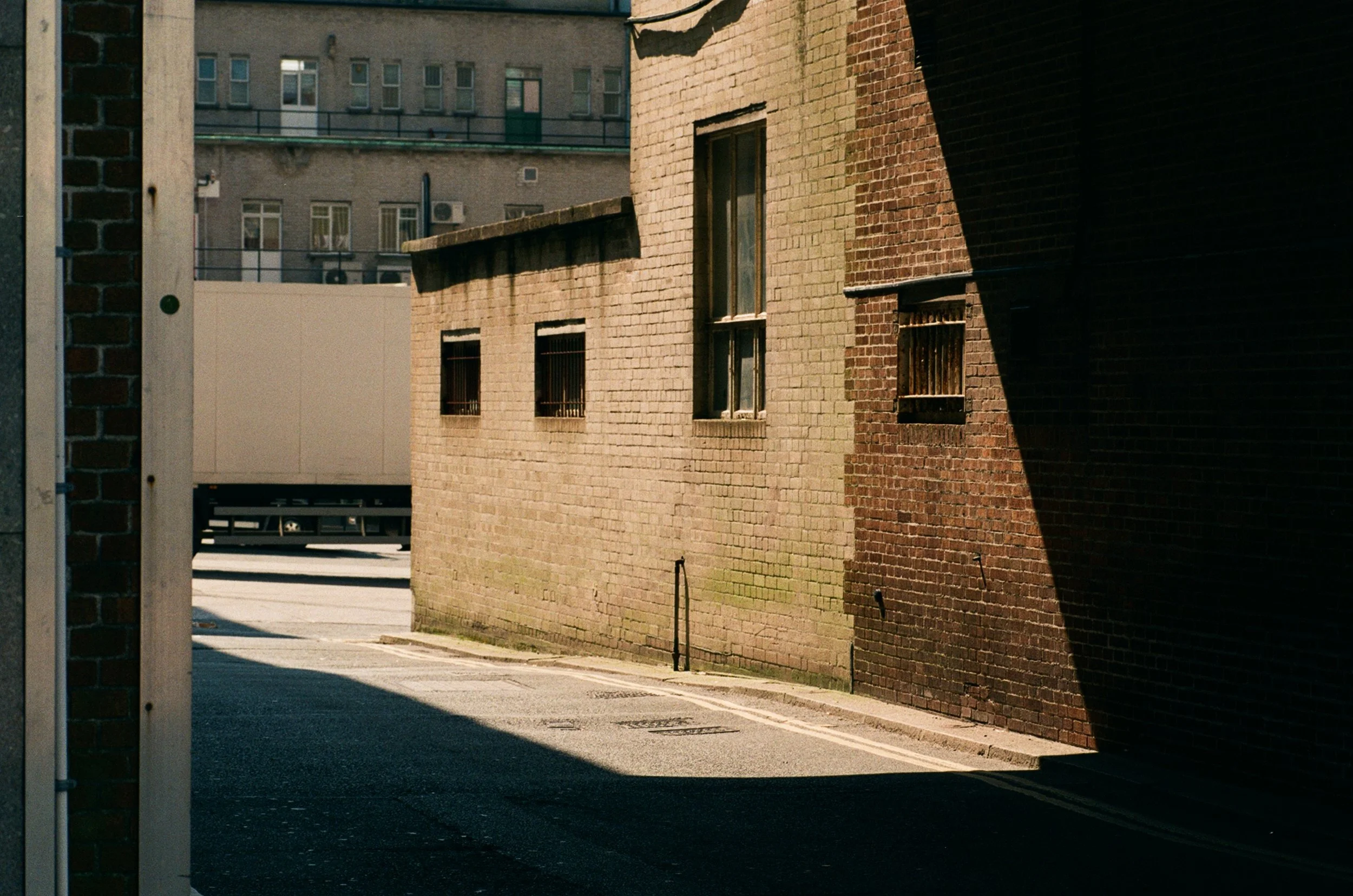 Sunlit brick building on a quiet urban street framed by deep architectural shadows in Plymouth, Devon