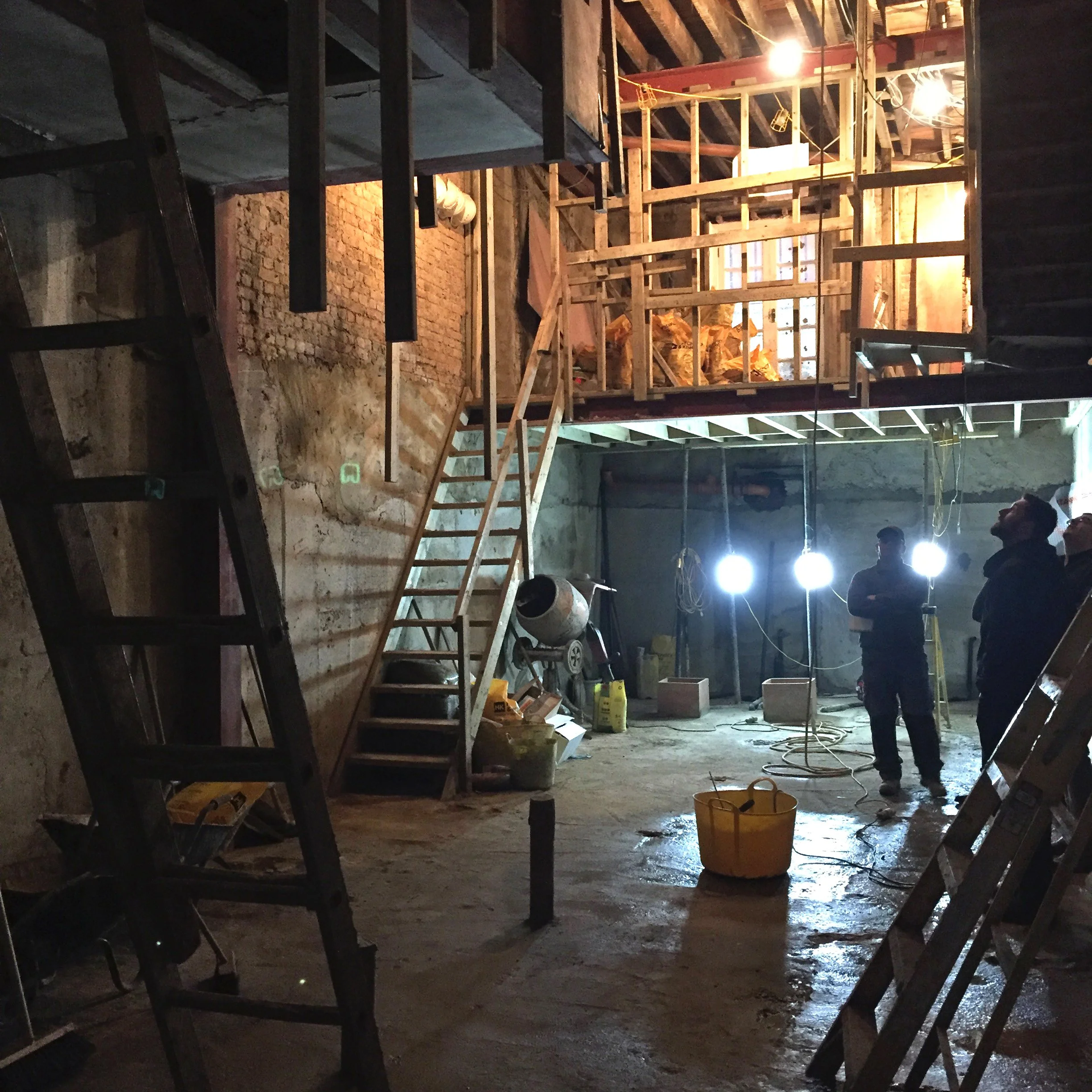 Construction photograph of a double-height Kensington basement showing timber, concrete and steel hybrid construction with members of the design team
