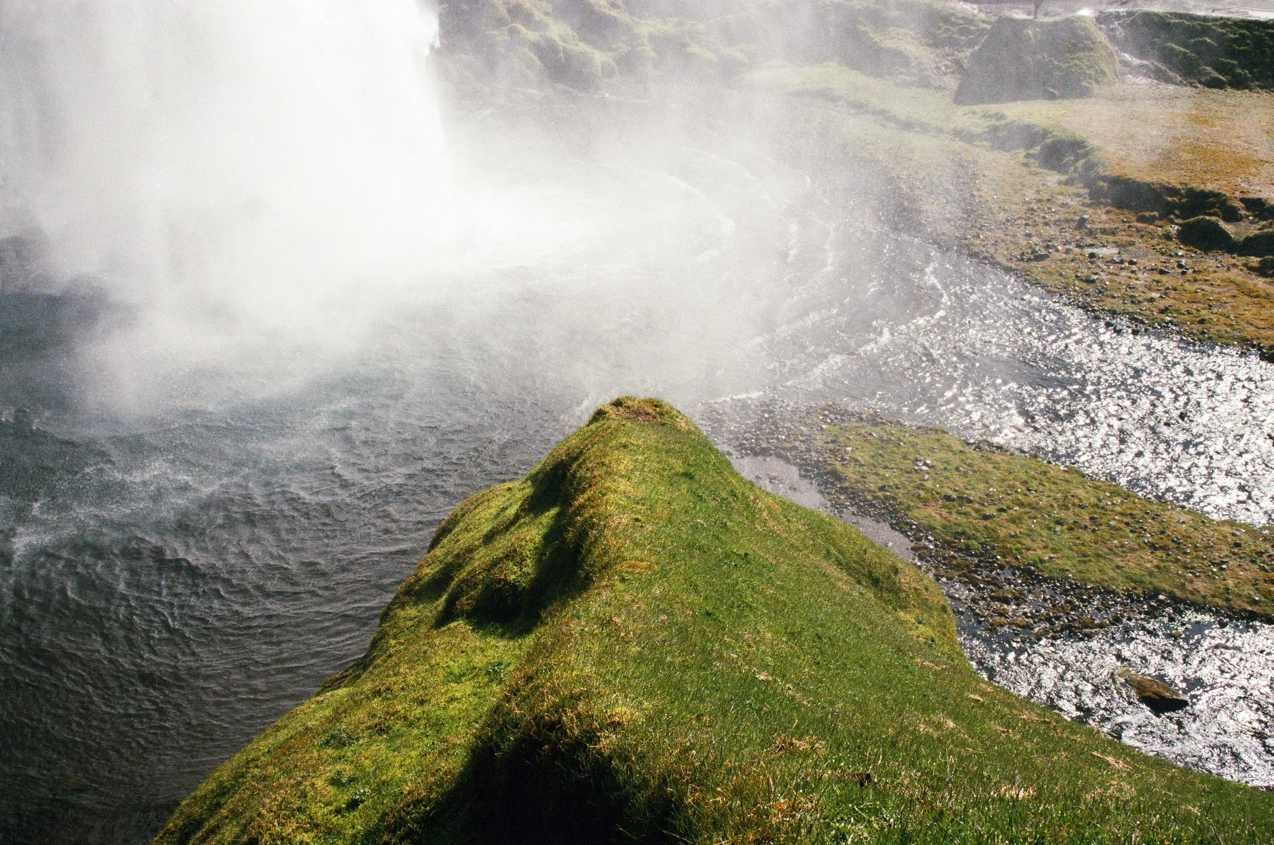 Moss-covered rock beside a waterfall surrounded by drifting spray in Iceland