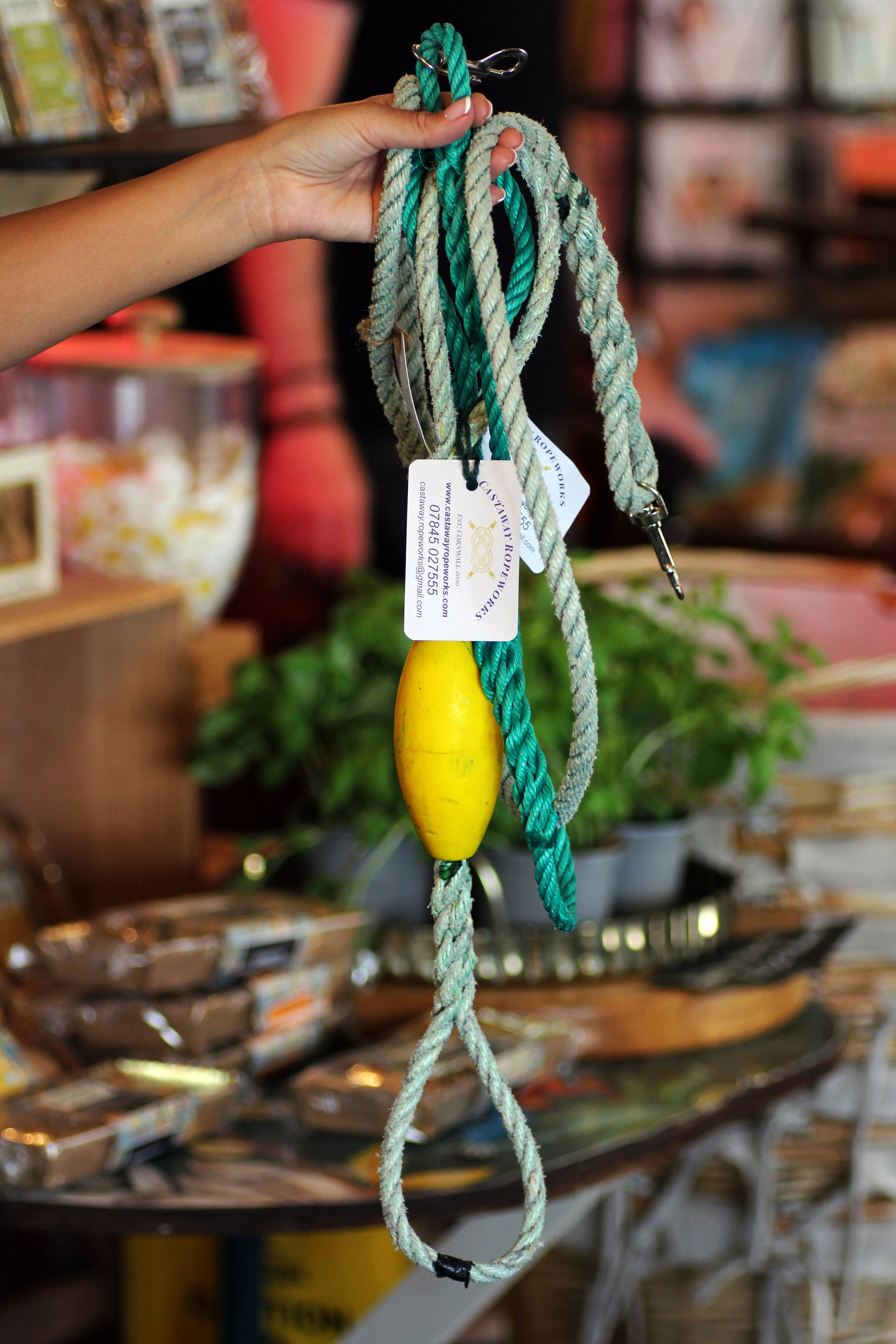 Hand holding a decorative nautical rope with a yellow float inside a shop in St. Agnes, Cornwall