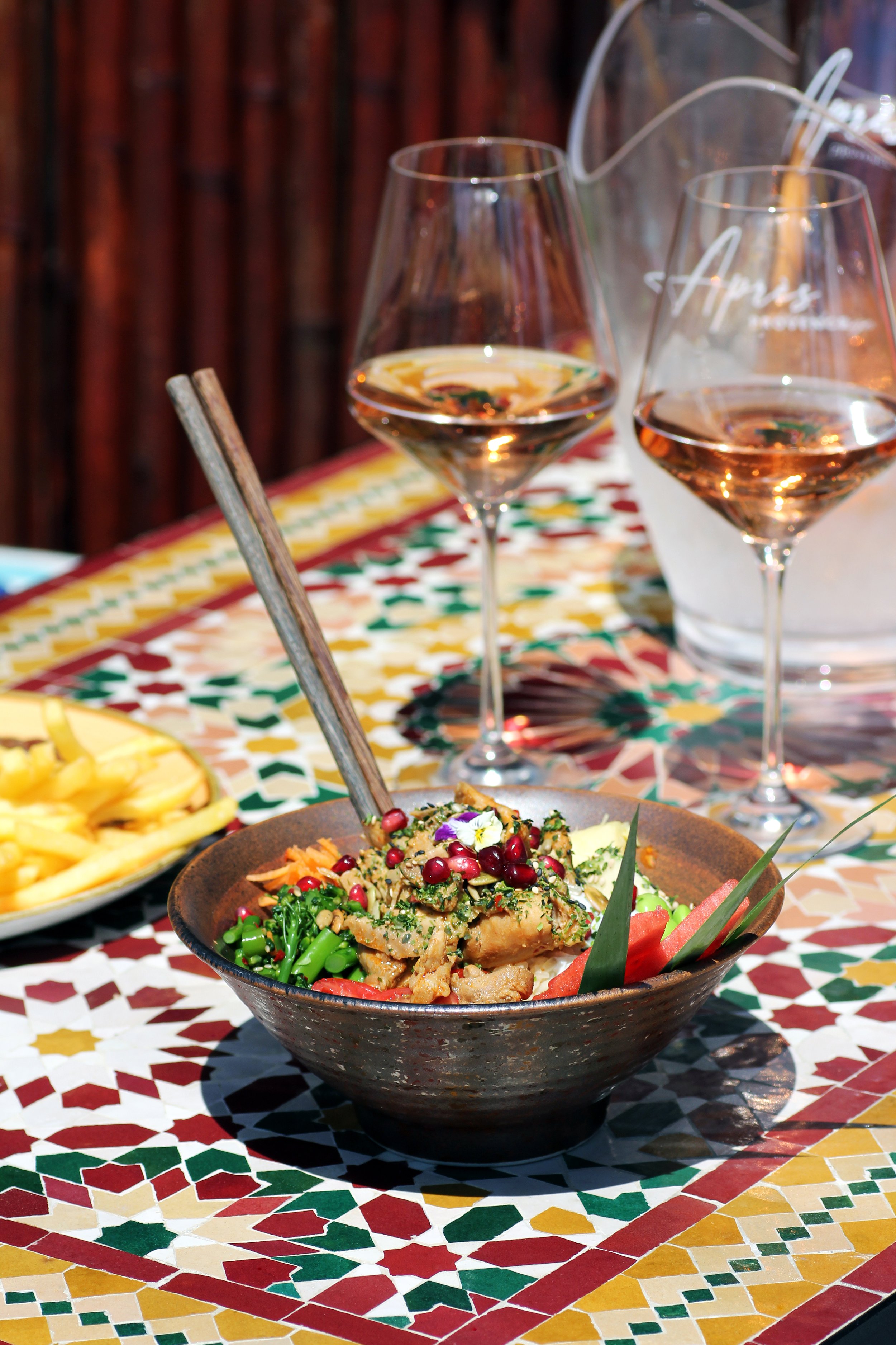Poke bowl on a colourful tiled table with two glasses of Apres wine at The Taphouse, St. Agnes, Cornwall