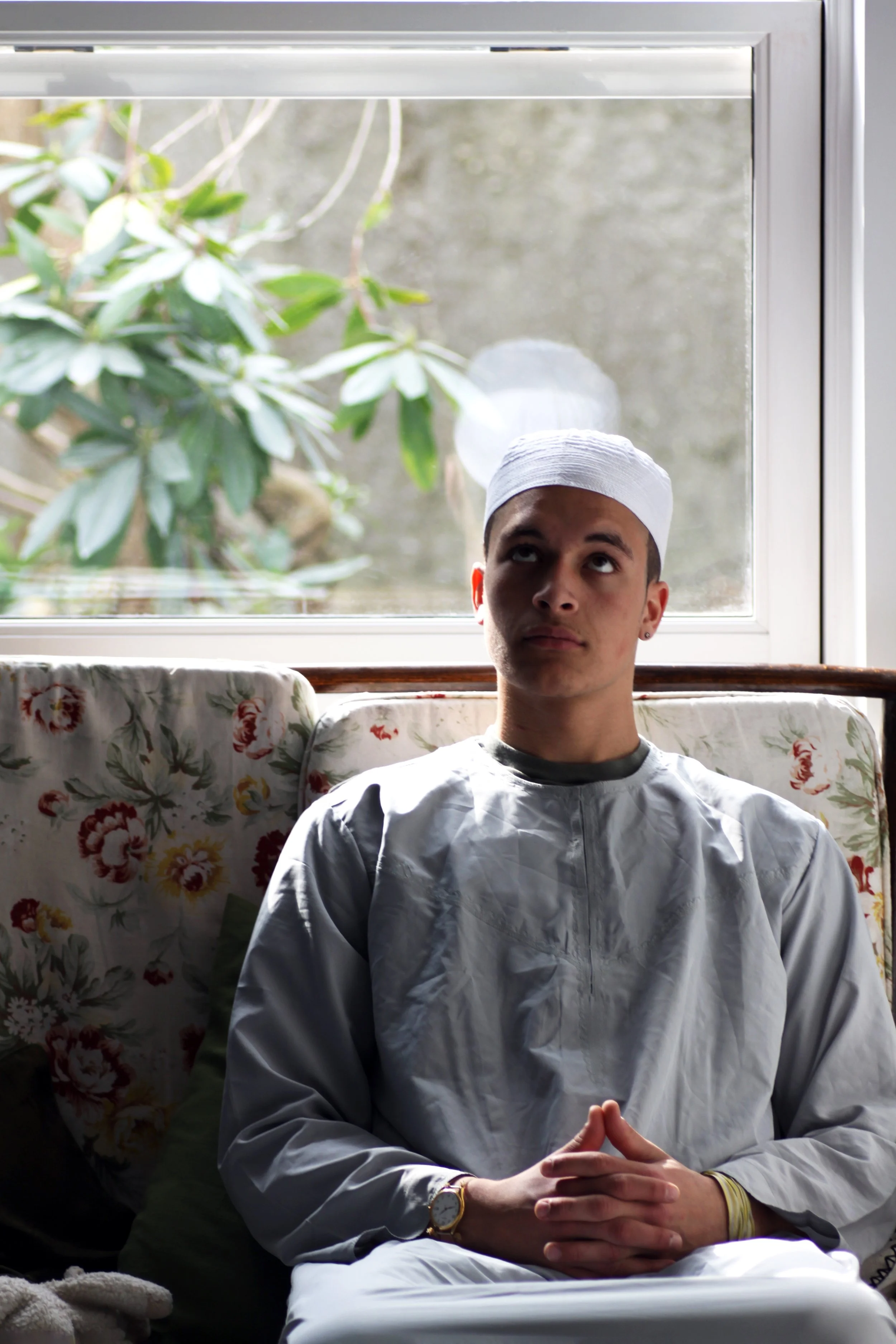 Shaahid seated by a window wearing a white thobe and kufi cap