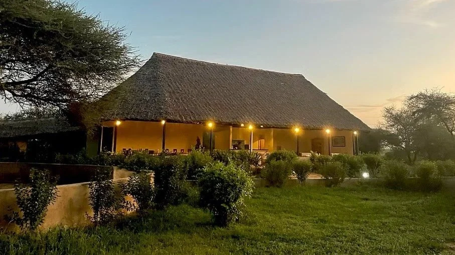 A thatched roof building with a porch surrounded by greenery and trees during sunset.