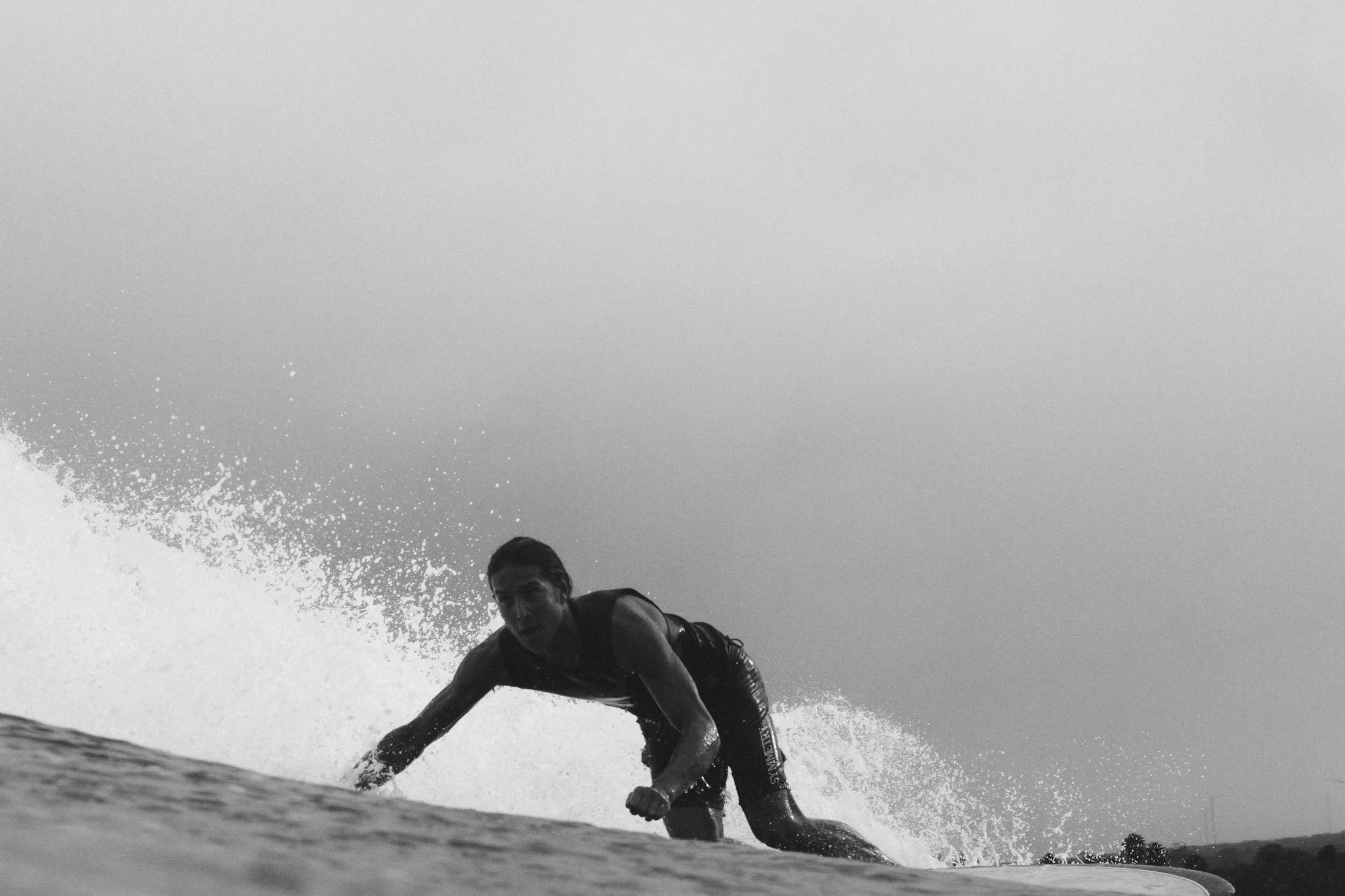 A person surfing on a wave, crouching low, with water splashing around, captured in black and white.