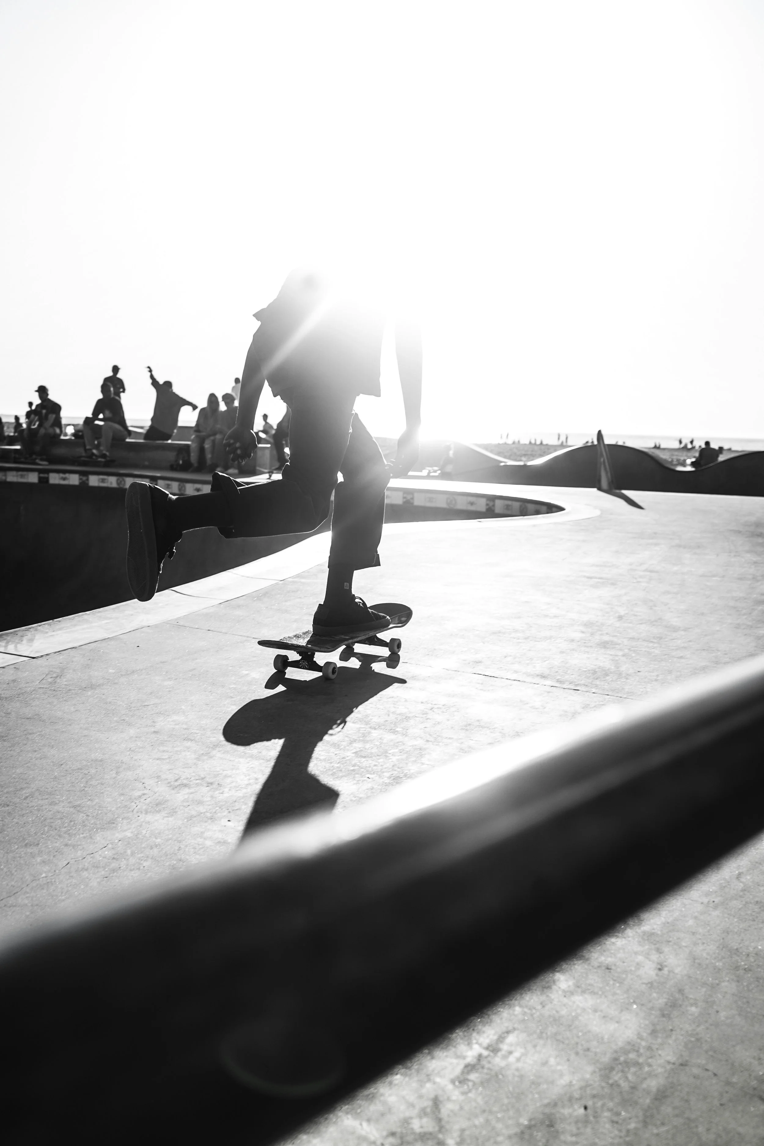 Skateboarder performing a trick at a skatepark during sunset, with several spectators in the background.