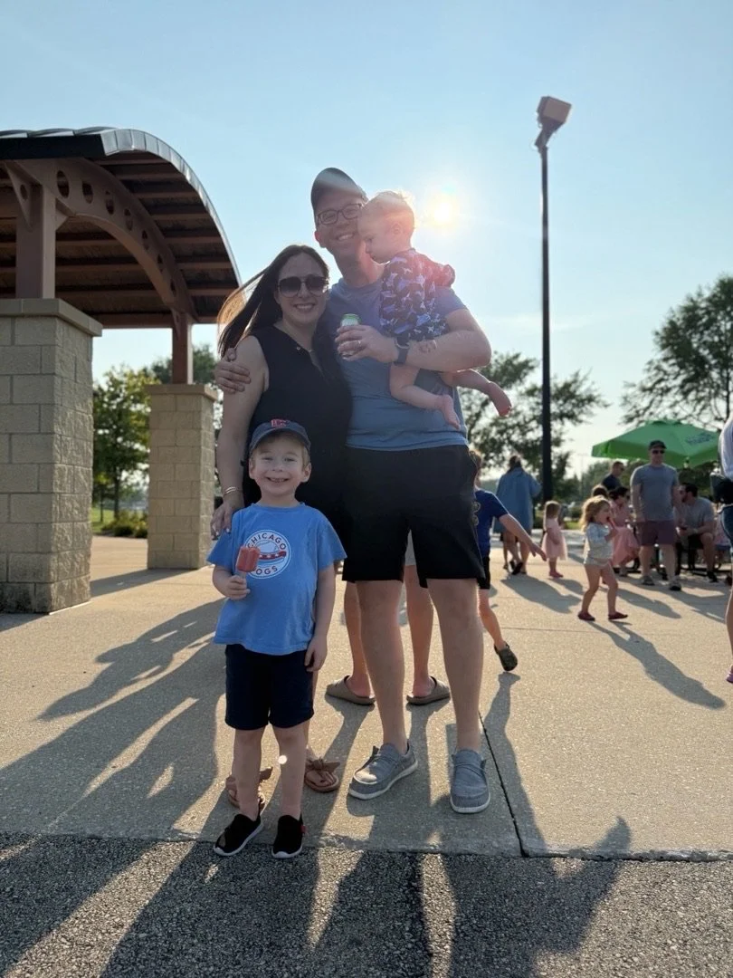 A family of four at an outdoor park during sunset, smiling and posing for the photo.