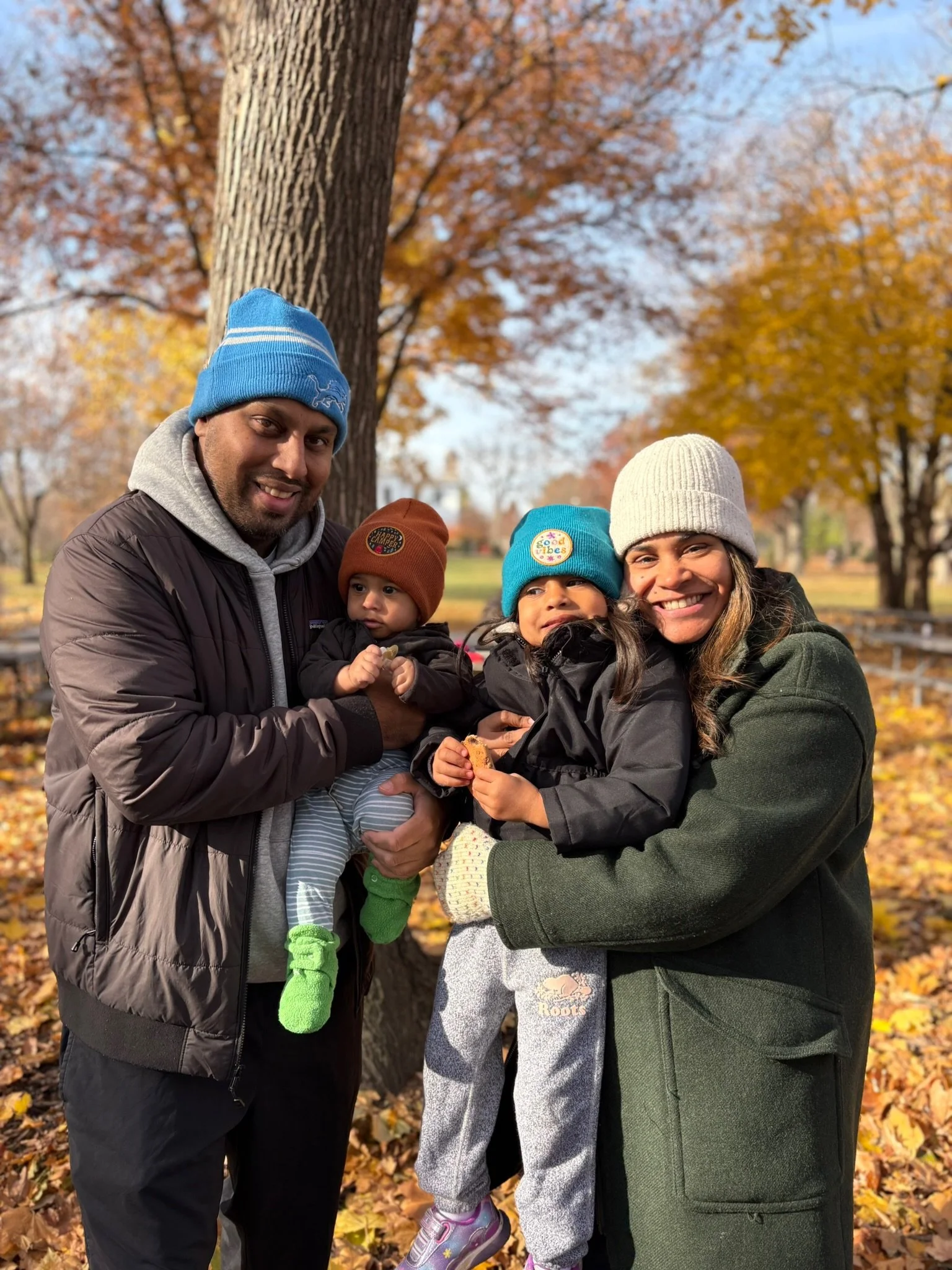 Family posing outdoors in fall with colorful trees in the background.