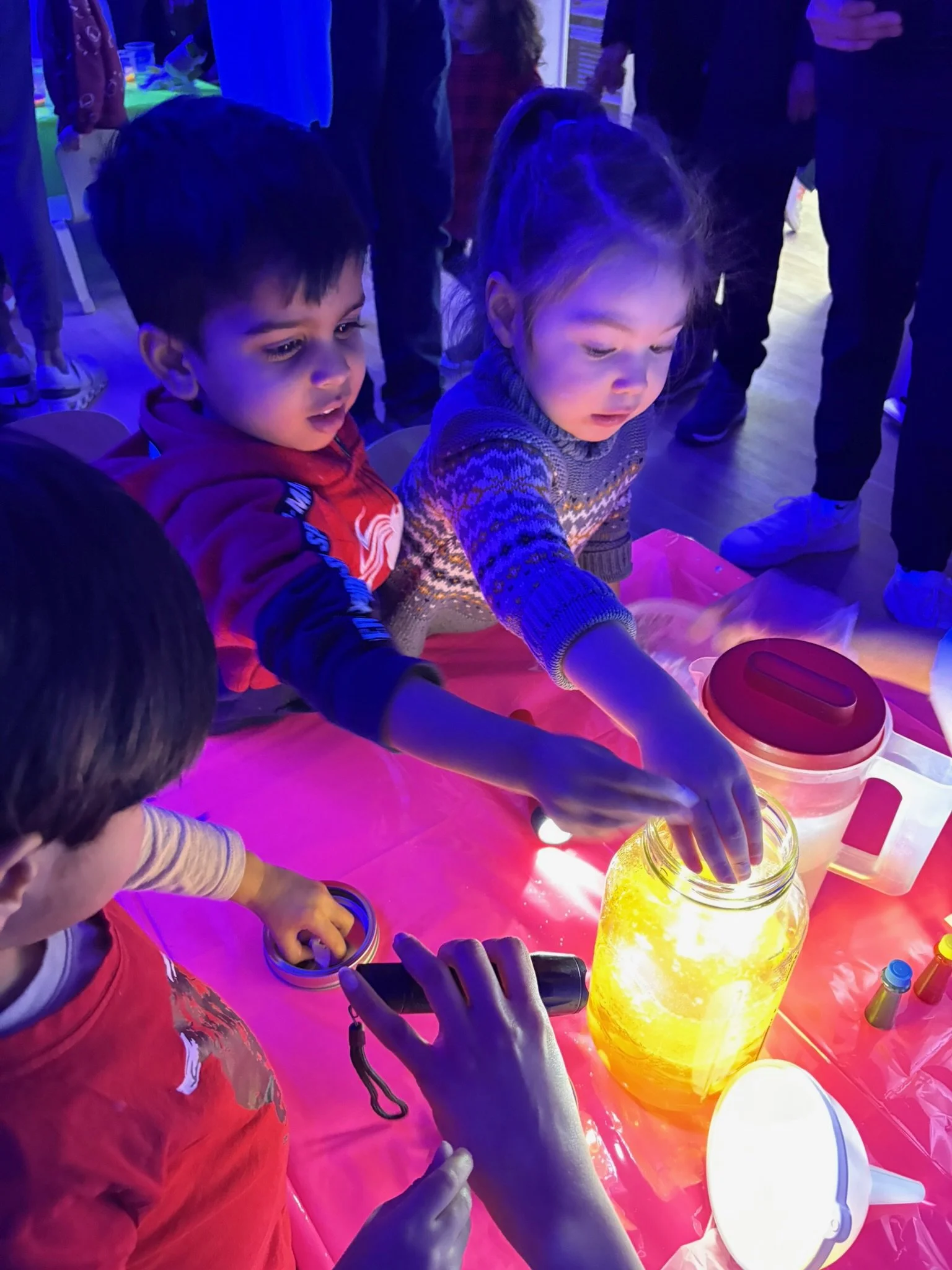 Children gathered around a glowing lemon-shaped lamp, reaching out and touching it during a nighttime event.