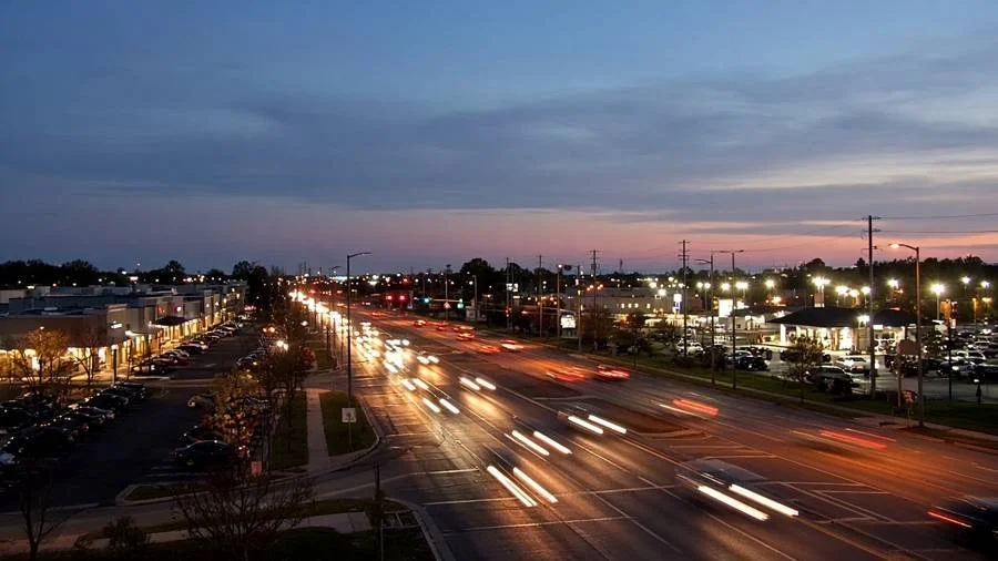 Busy suburban road with shopping plazas at evening (illustration)