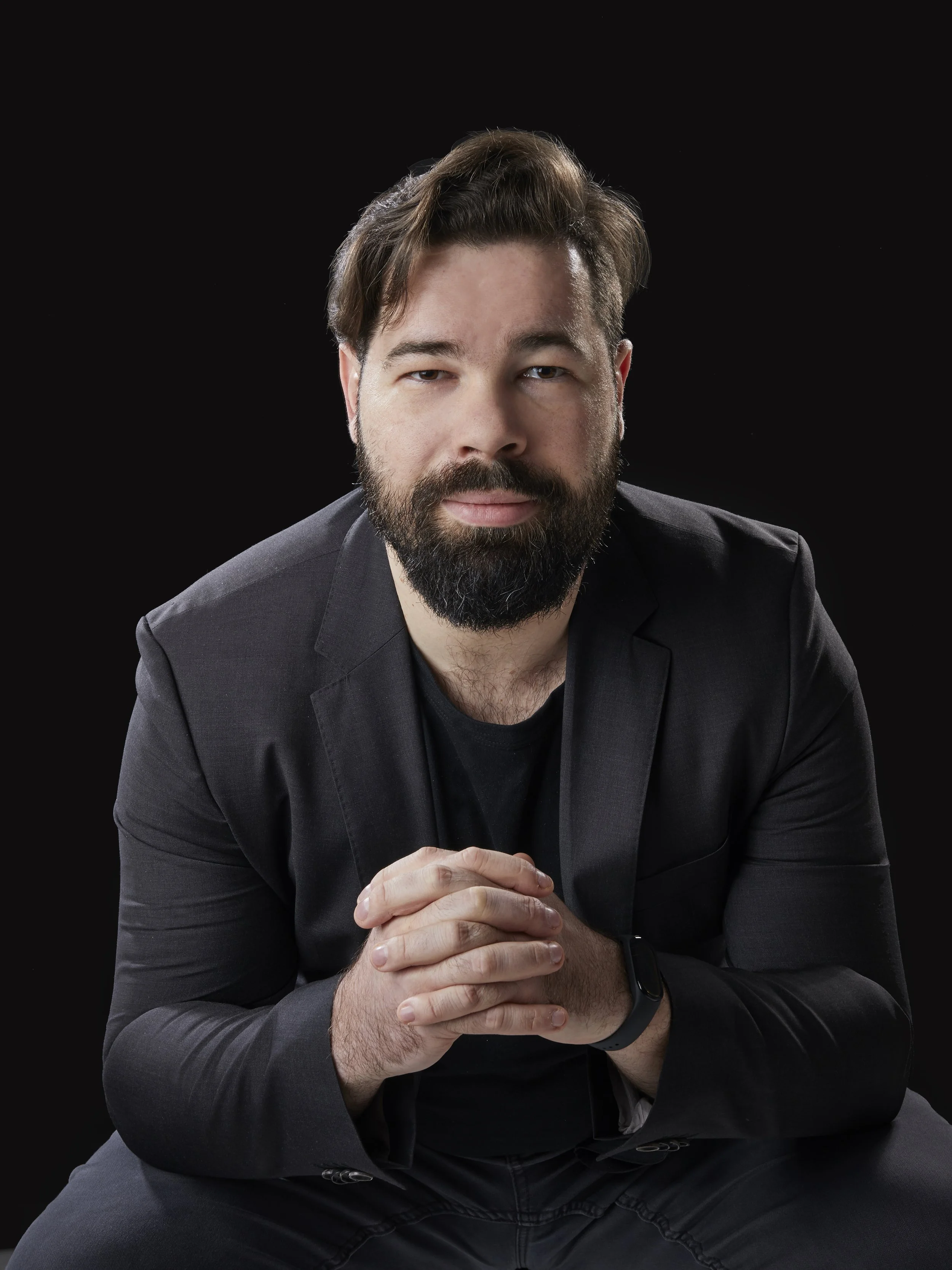 Porträt eines Mannes mit dunklem Anzug und lockigem Haar auf schwarzem Hintergrund.