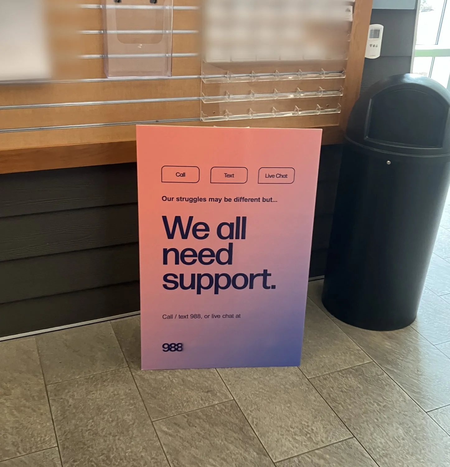Crisis-line standee on the floor of a community center lobby beside a trash bin