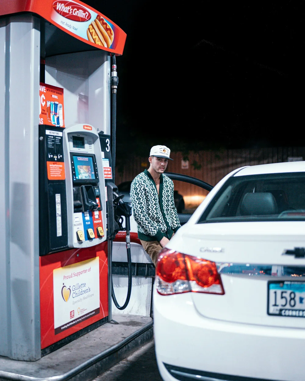 Driver fueling up at night beside a pump with an ad topper