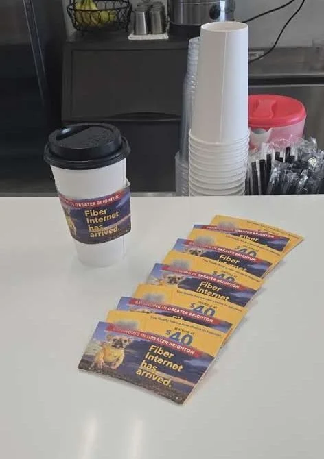 Coffee cup with a branded sleeve beside a fanned stack of take-one cards on a cafe counter