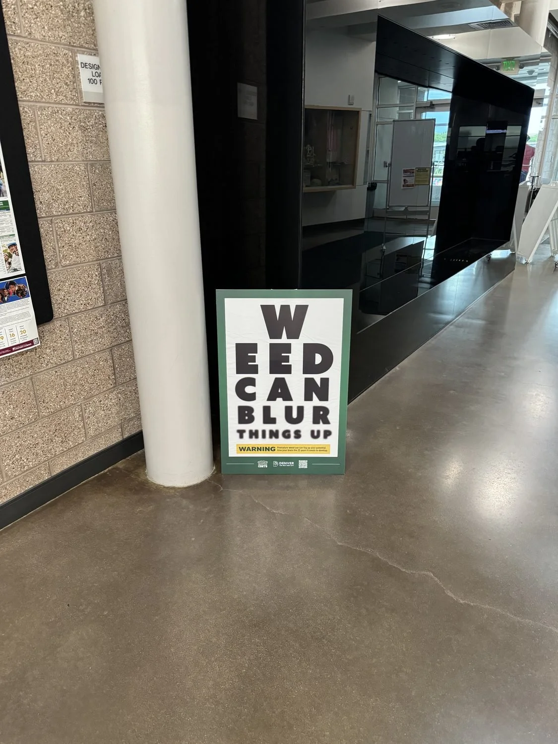 Weed Can Blur Things Up cannabis-prevention floor poster standing in a school hallway beside a white column