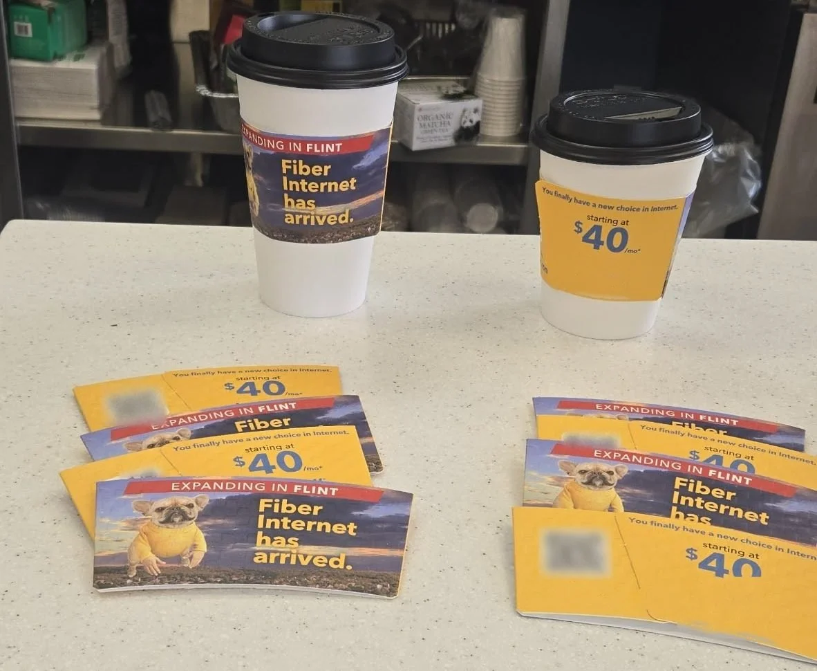 Branded coffee sleeves on hot cups beside stacks of matching counter cards on a cafe counter