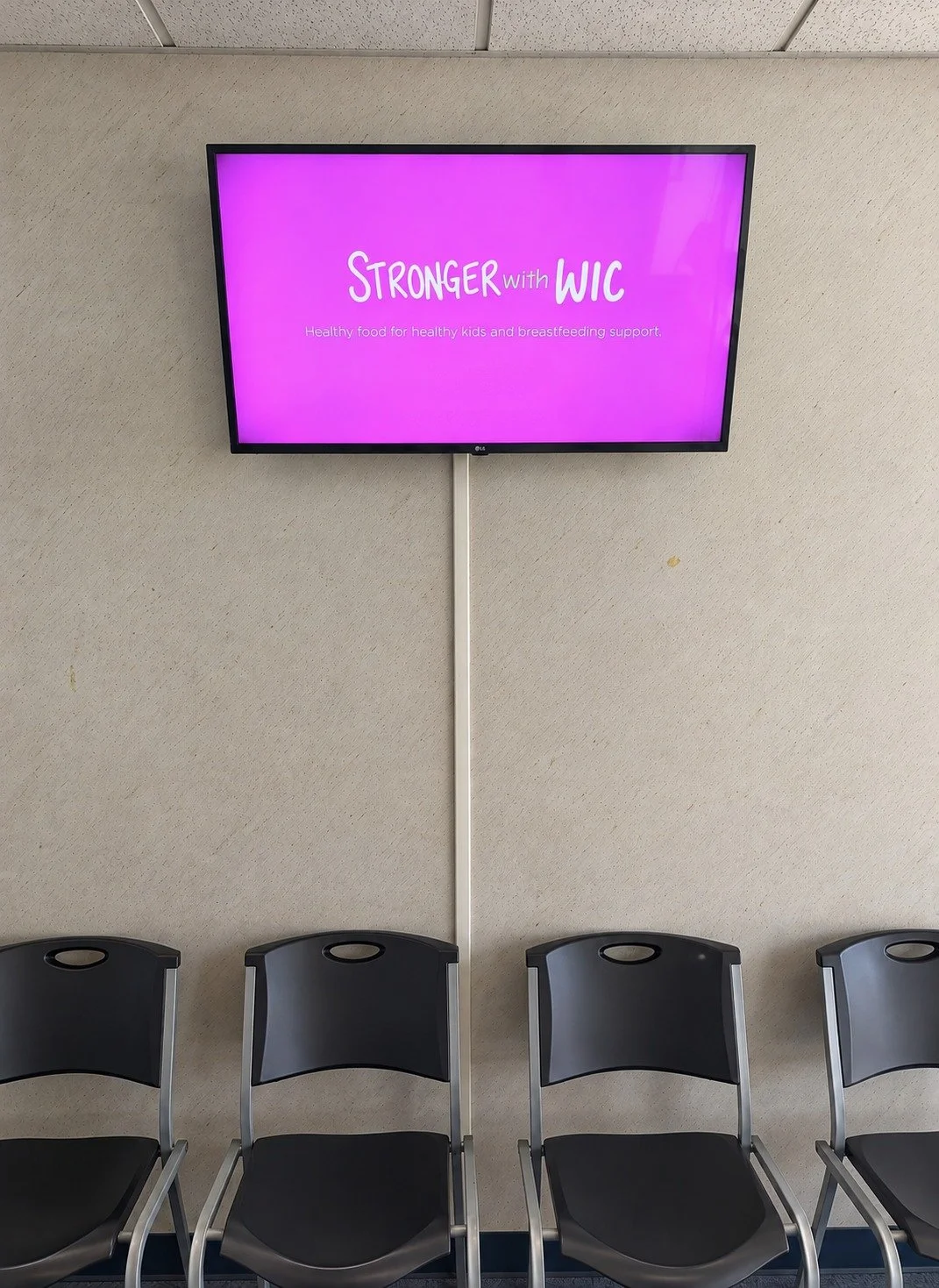 Digital screen showing a WIC healthy food message above clinic waiting room chairs