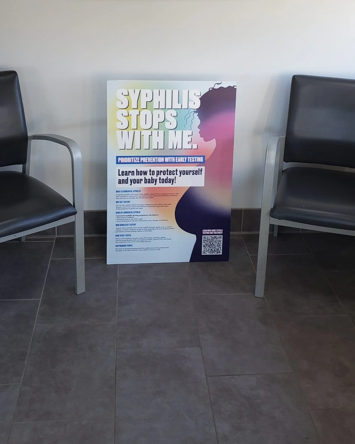 Syphilis prevention poster encouraging early testing during pregnancy, standing between chairs in a clinic waiting room