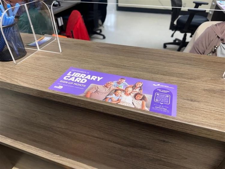 Purple Library Card Sign-Up Month counter mat on a school front-office desk