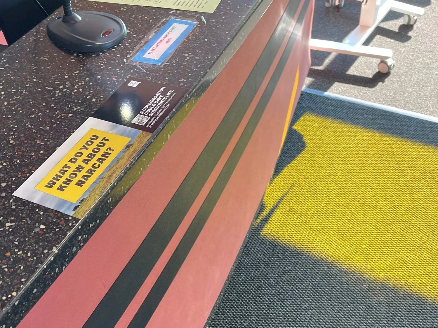 Counter mat with a naloxone-awareness message on a community center front desk