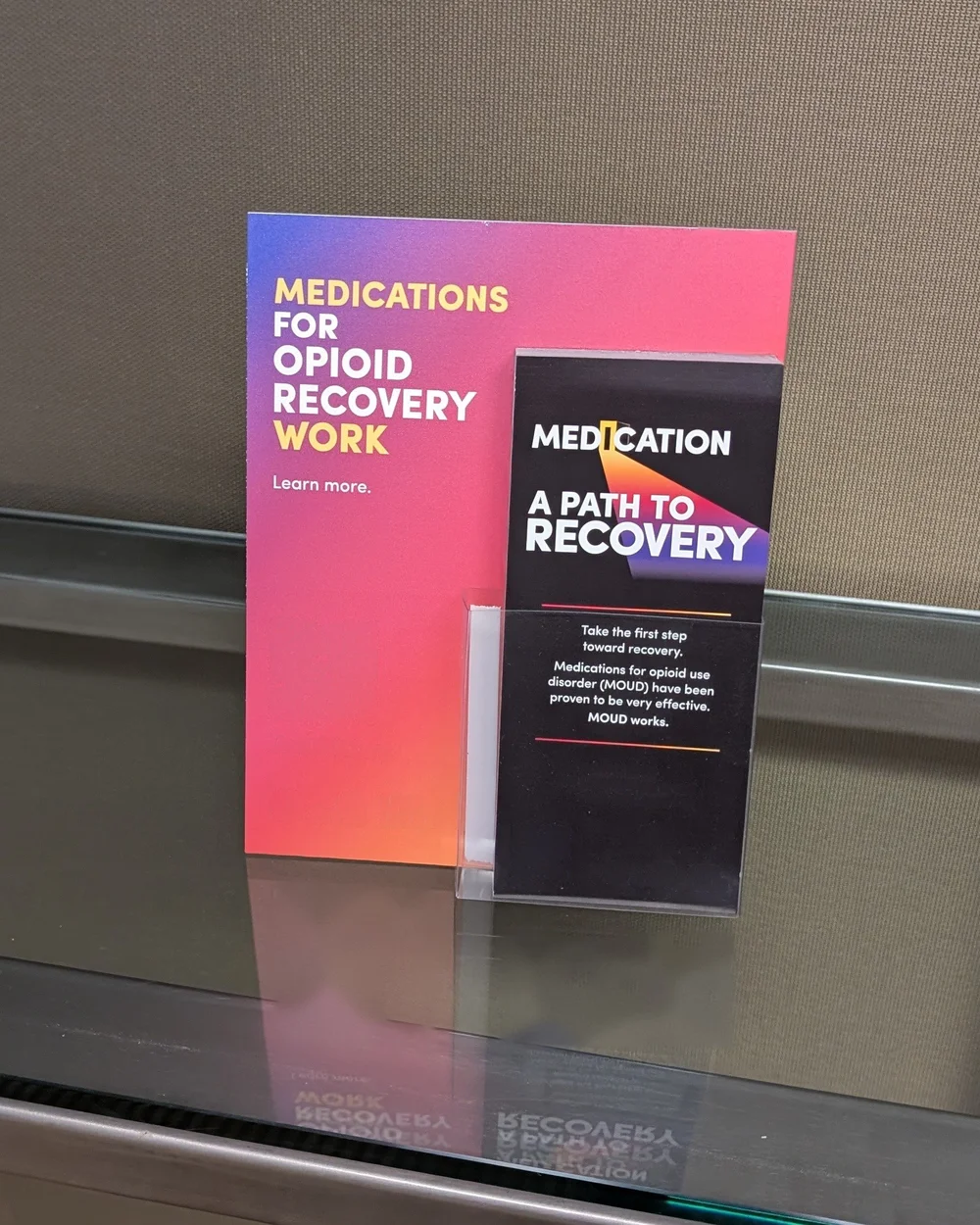Opioid recovery take-one cards in an acrylic holder in front of a matching sign on a glass ledge