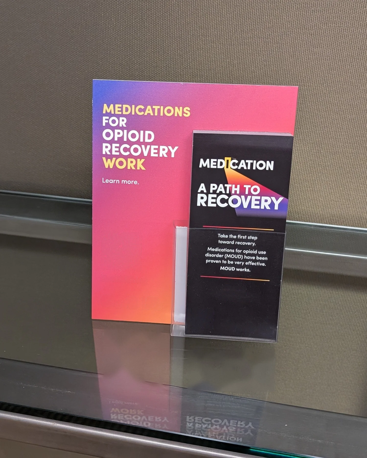 Opioid recovery take-one cards in an acrylic holder in front of a matching sign on a glass ledge
