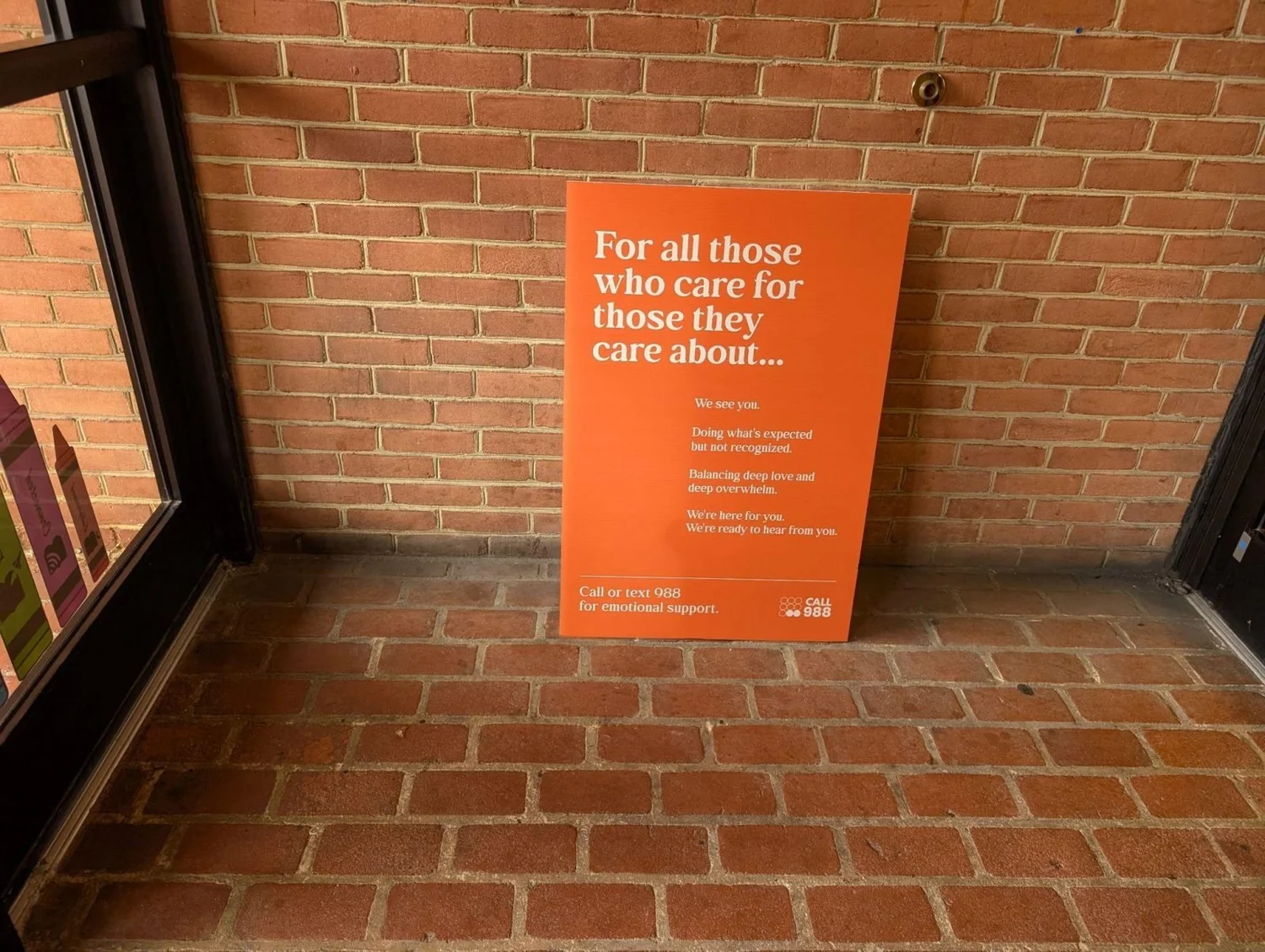 Caregiver support standee for the 988 lifeline against a brick wall in a coffee shop entryway