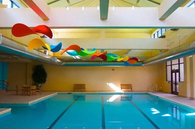 Indoor swimming pool with colorful abstract art installation hanging from the ceiling.