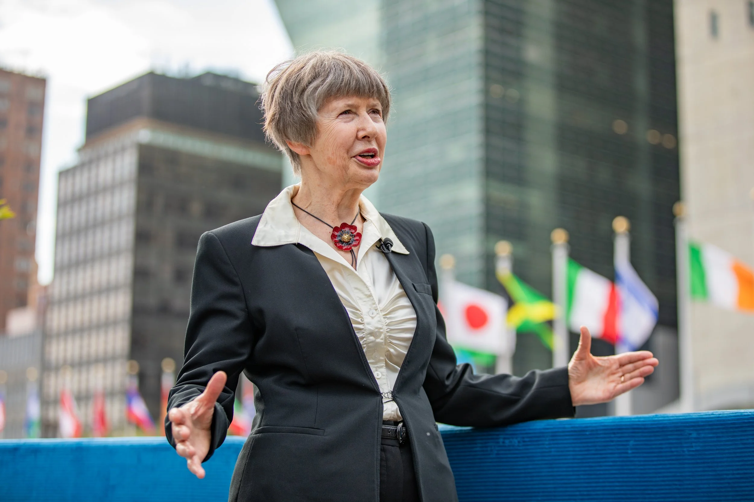 A man with glasses and a beard, dressed in a gray plaid blazer and light blue shirt, sitting in a room with a window and a flower arrangement in the background.