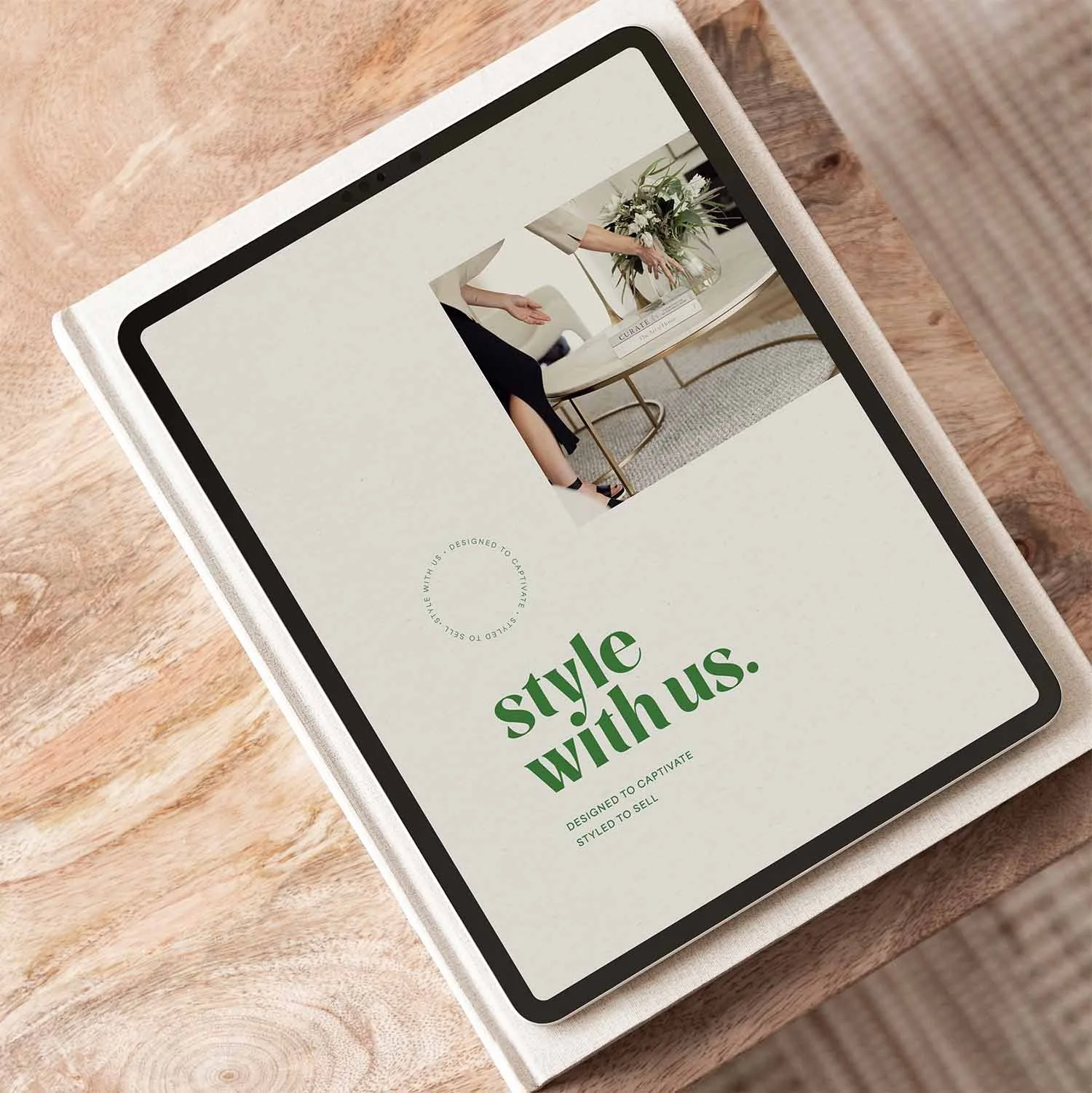 An iPad showing the aligned brand refresh for Style With Us Property Styling, designed by Indeko Creative,  sits on top of a book and a timber table above a modern neutral rug.