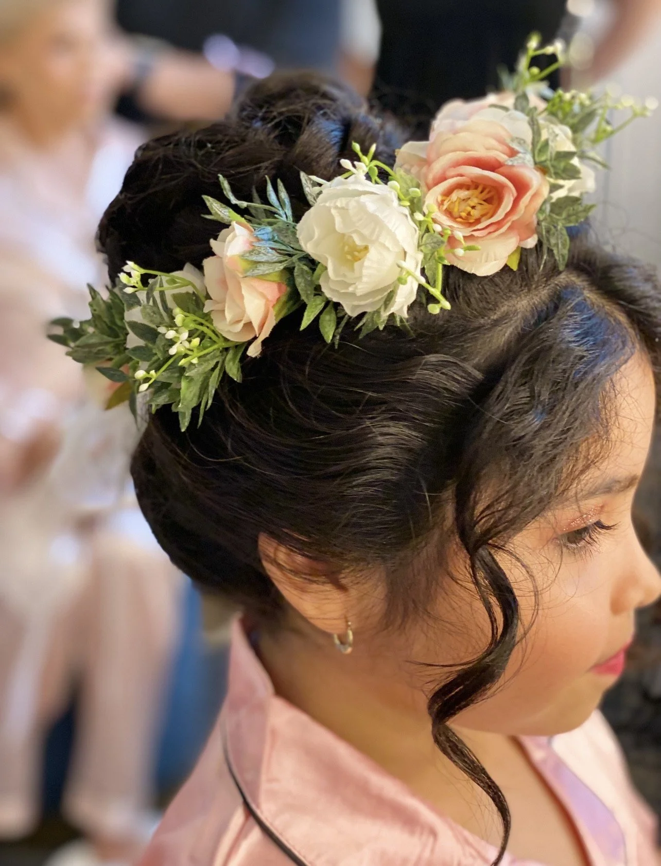 A young girl with reddish hair wearing a white dress holding a bouquet of purple and white wildflowers in a green outdoor setting.