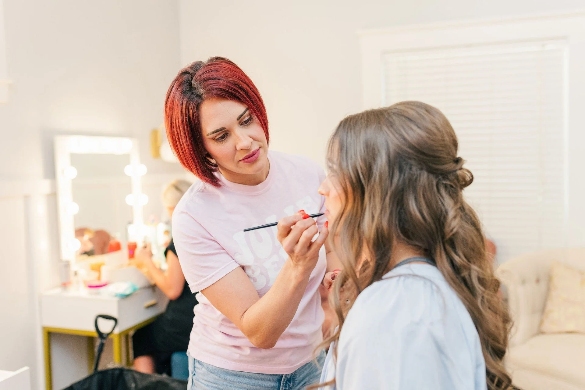 Makeup artist applying makeup on a woman with dark hair and a decorative hairpiece.