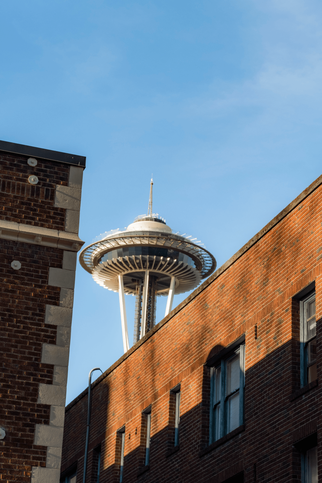 The Seattle Space Needle viewed from between two brick buildings on a clear day with blue sky.