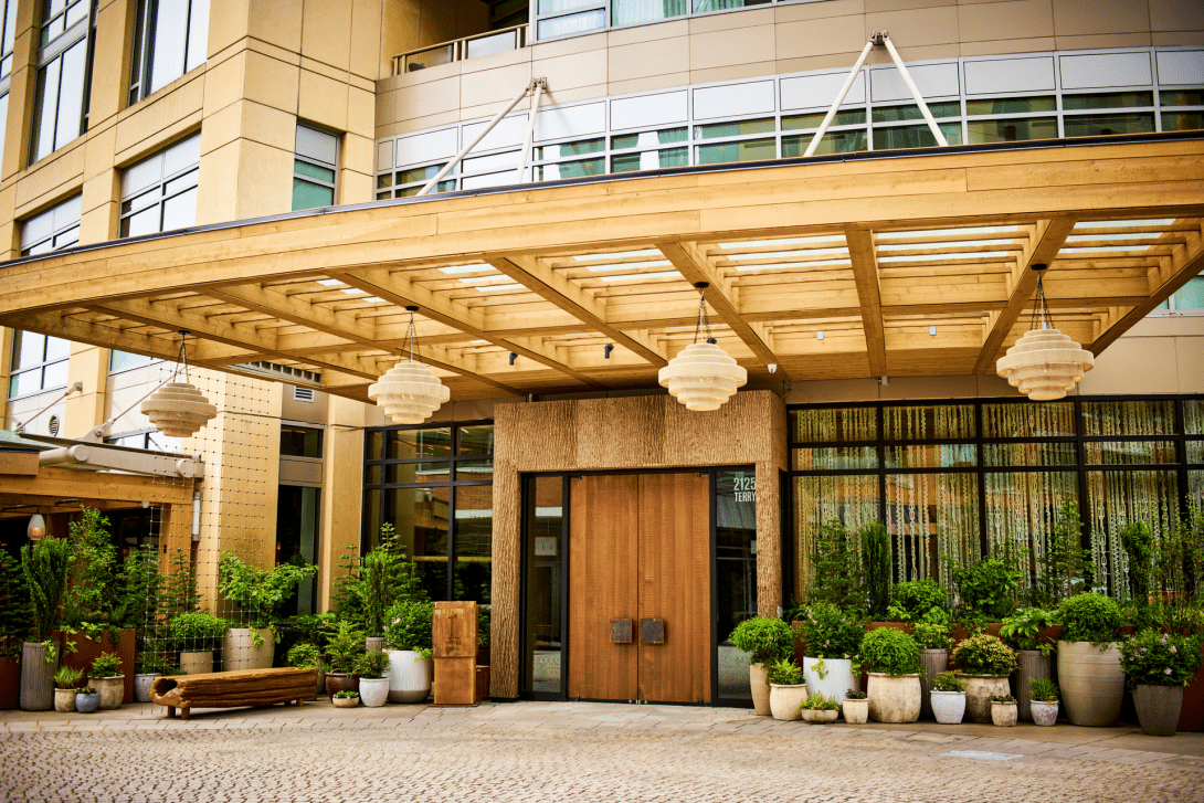 Exterior entrance of a modern building with a wooden canopy, hanging lamps, and potted plants.